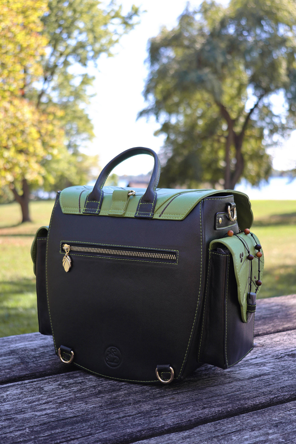 Dark brown and green bag on a wooden surface with trees and grass in the background