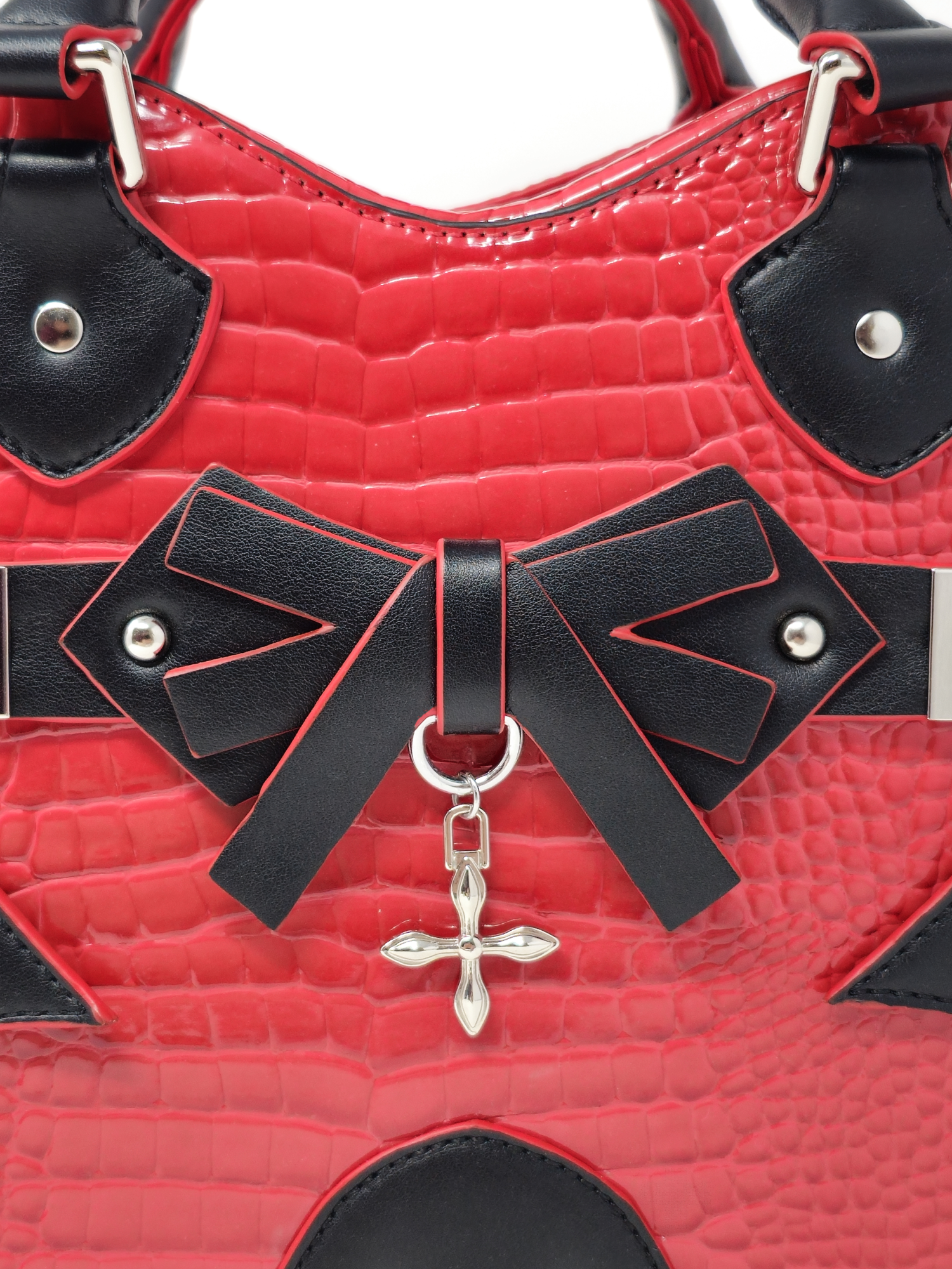 Close-up of gothic heart bag with black faux leather bow and silver cross charm on red snakeskin texture