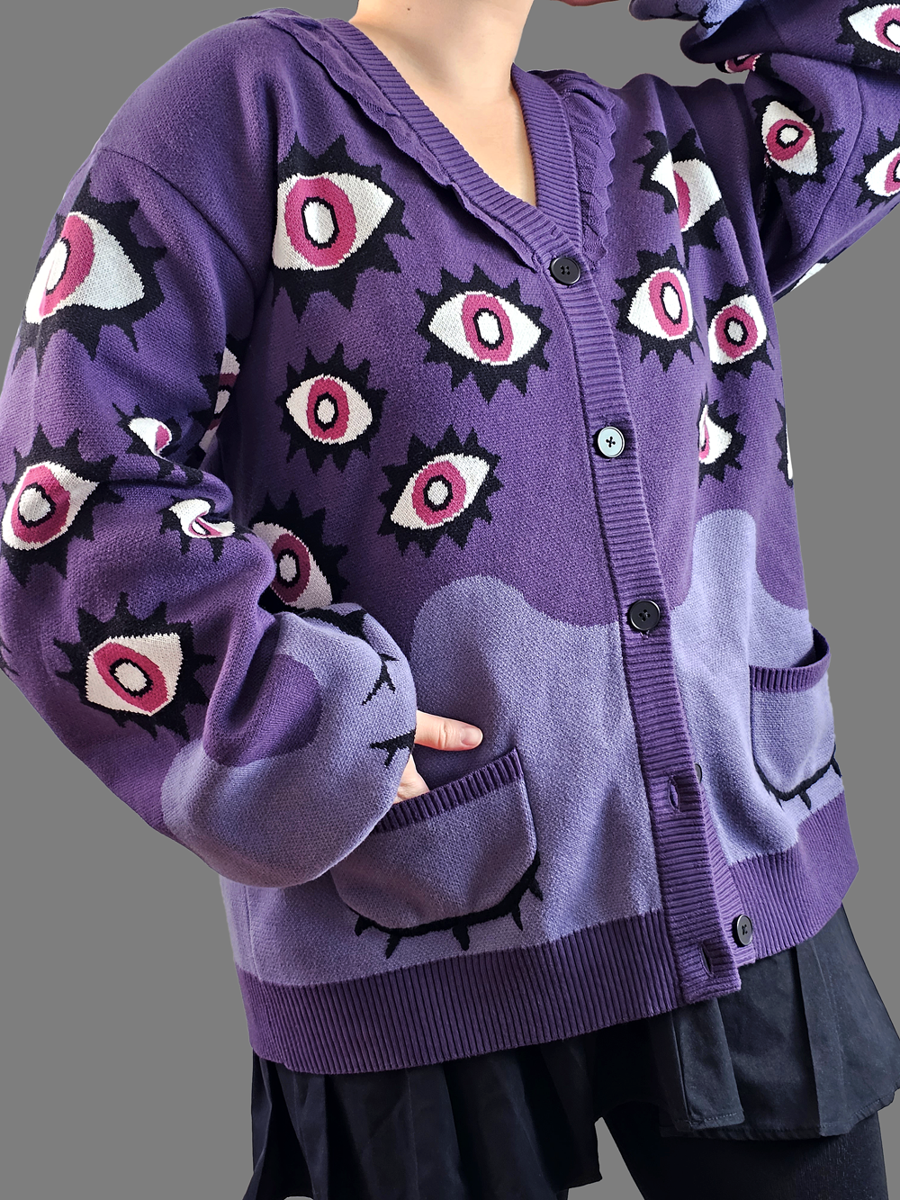 Close-up of model wearing the Abyss Cardigan in purple, featuring bold pink eye motifs on an oversized 100% cotton knit.