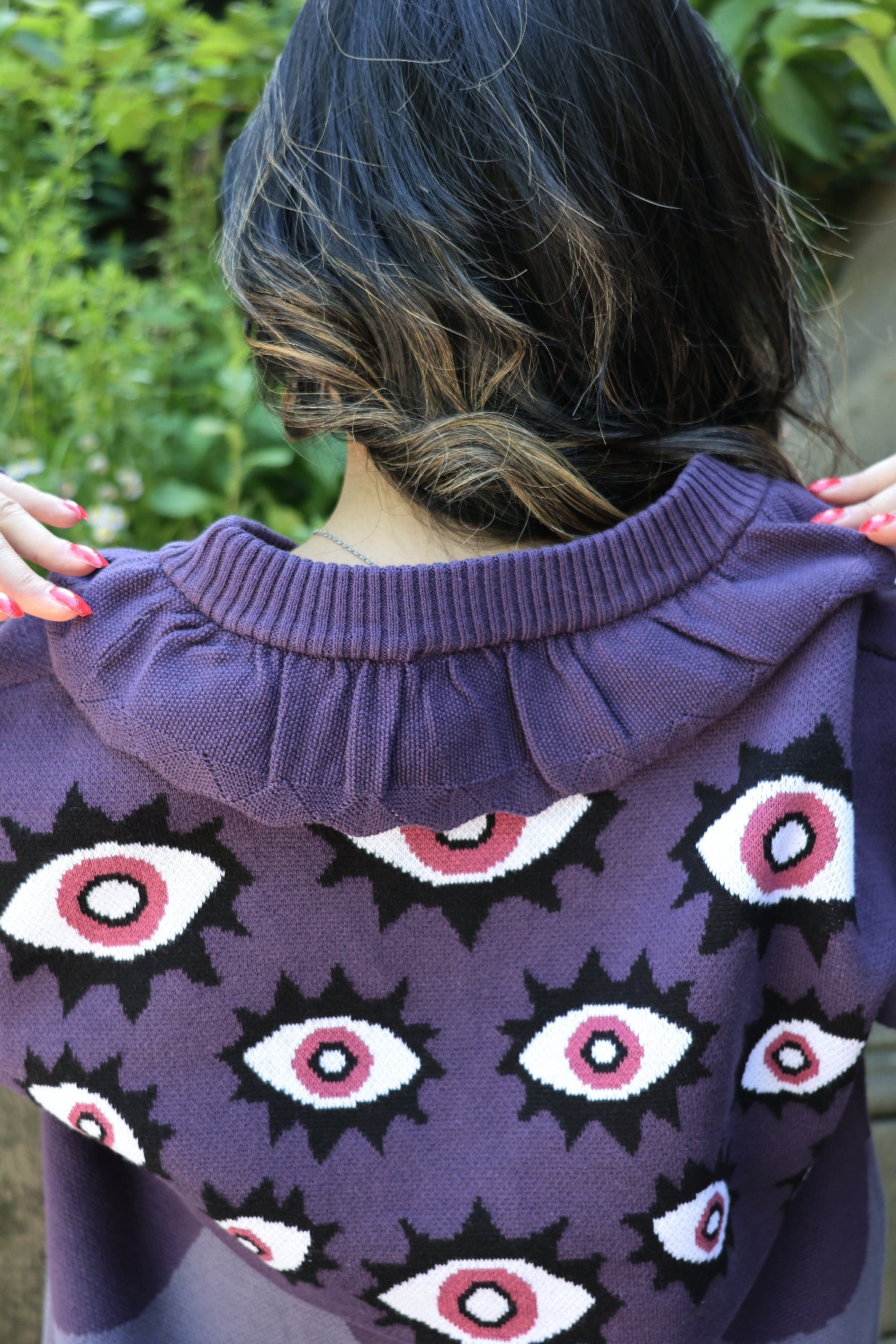 Close-up back view of the Abyss Cardigan showing the all-over pink and white eyeball knit pattern, ruffled collar detail, and oversized purple silhouette.