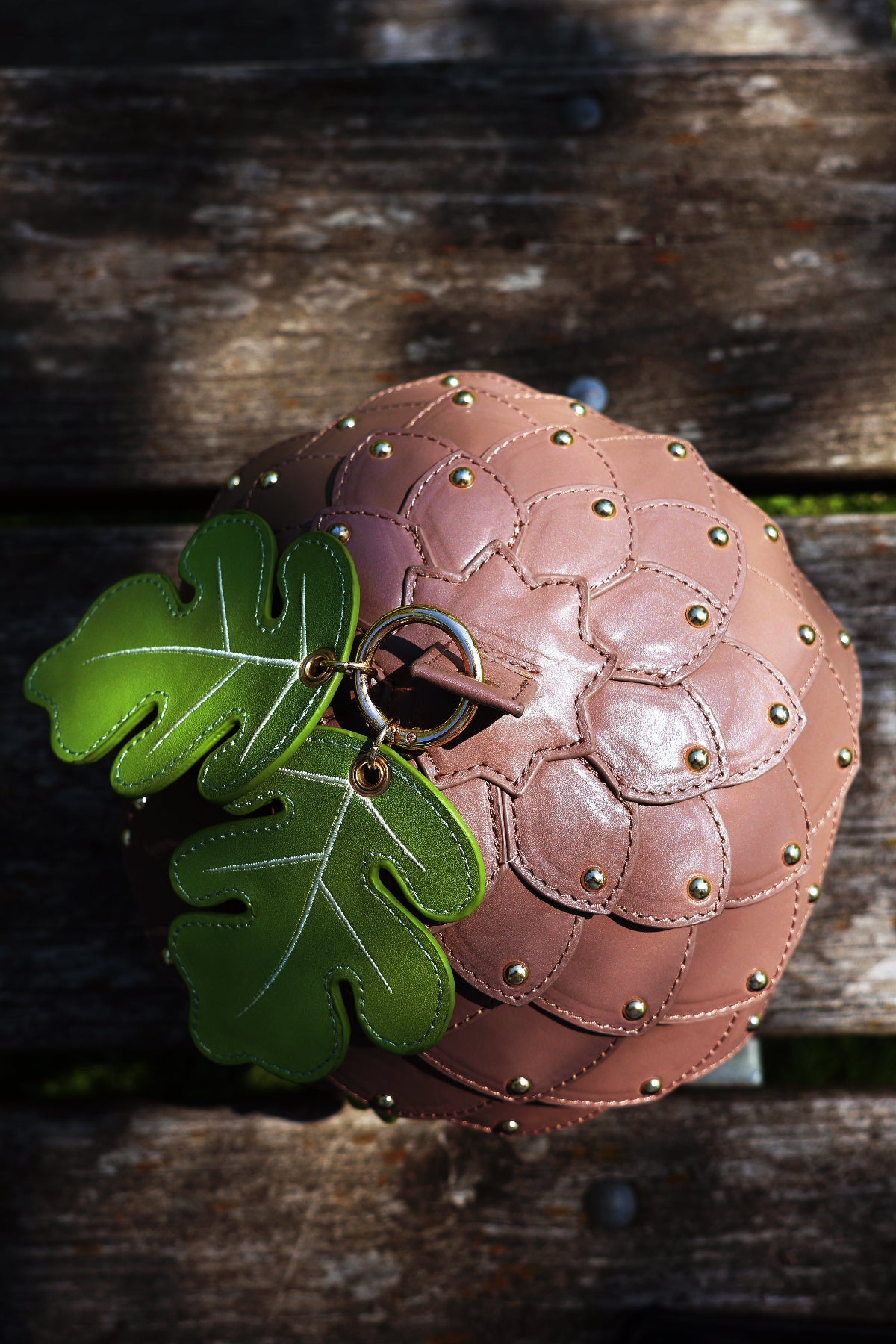 Top-down view of an acorn-shaped fantasy crossbody bag with layered acorn scale details, oak leaf charms, and gold rivets displayed on a rustic wooden table.