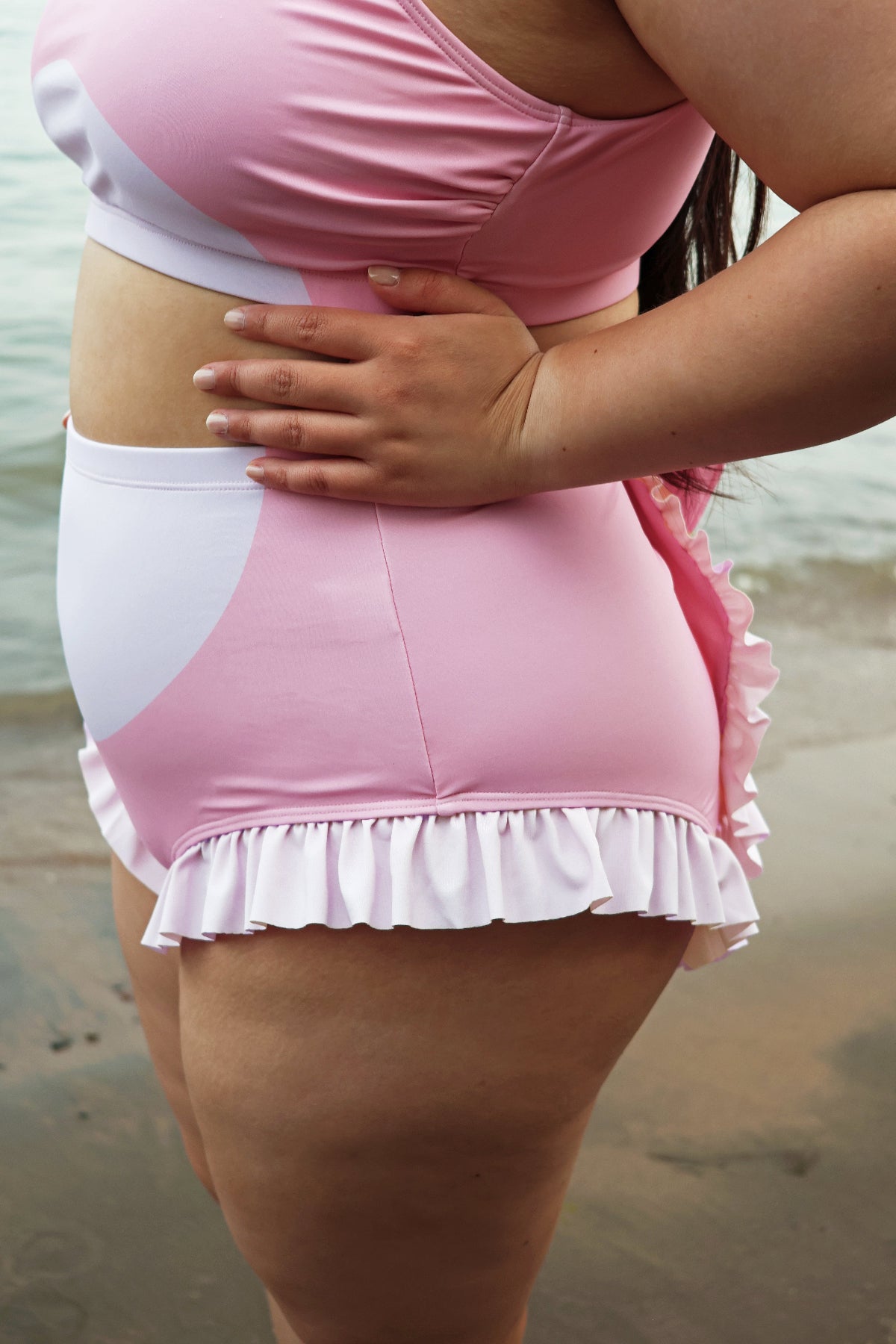 Close-up of the pink Axolotl swimsuit showing the high-waisted bikini bottoms with white belly detail and ruffled trim.