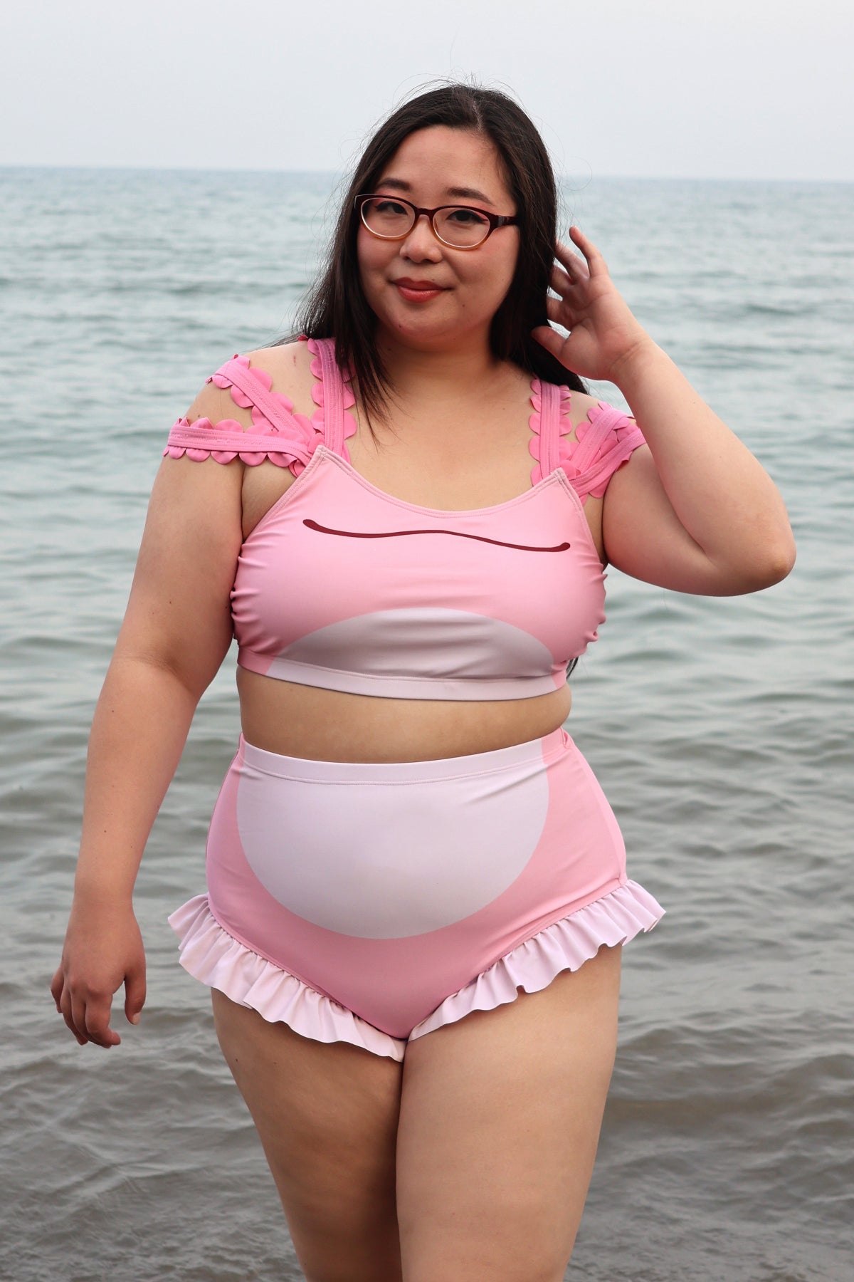 Model wearing the pink Axolotl two-piece swimsuit, featuring a cute axolotl-inspired swim top with decorative shoulder details and high-waisted ruffle-trim bikini bottoms.