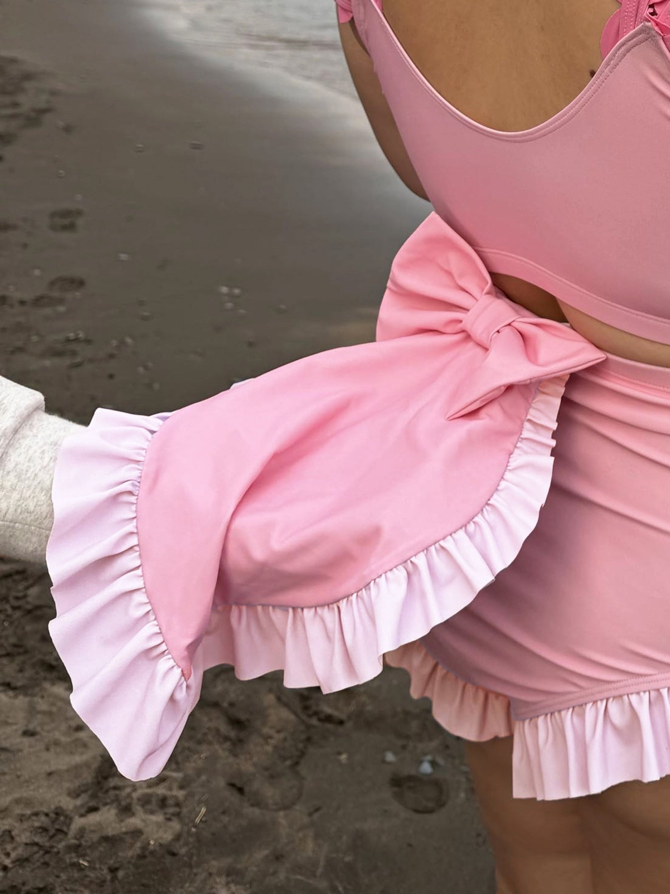 Close-up of the pink Axolotl swimsuit with matching wrap skirt, featuring a large side bow and soft ruffle trim.