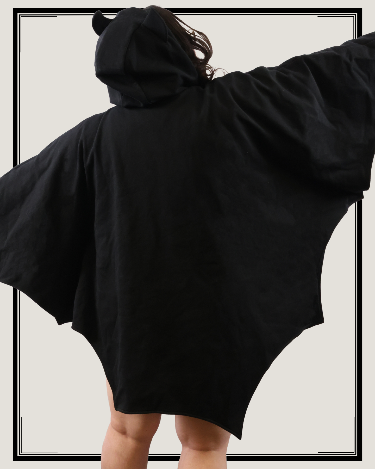 Back view of model wearing a black bat-inspired hooded cloak with arms extended to show wing-shaped silhouette against a light background
