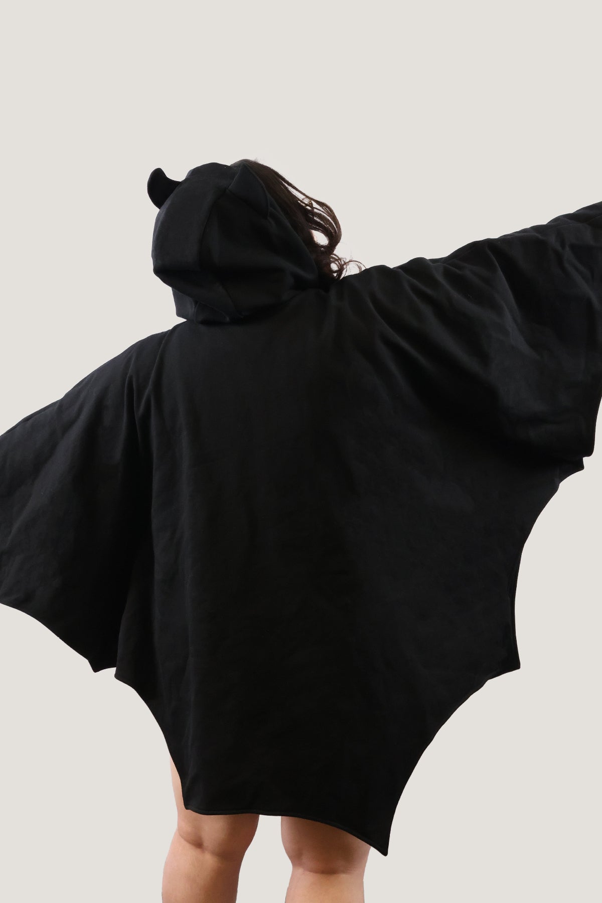 Back view of model wearing a black bat-inspired hooded cloak with arms extended, showing full wing-like silhouette against a light background