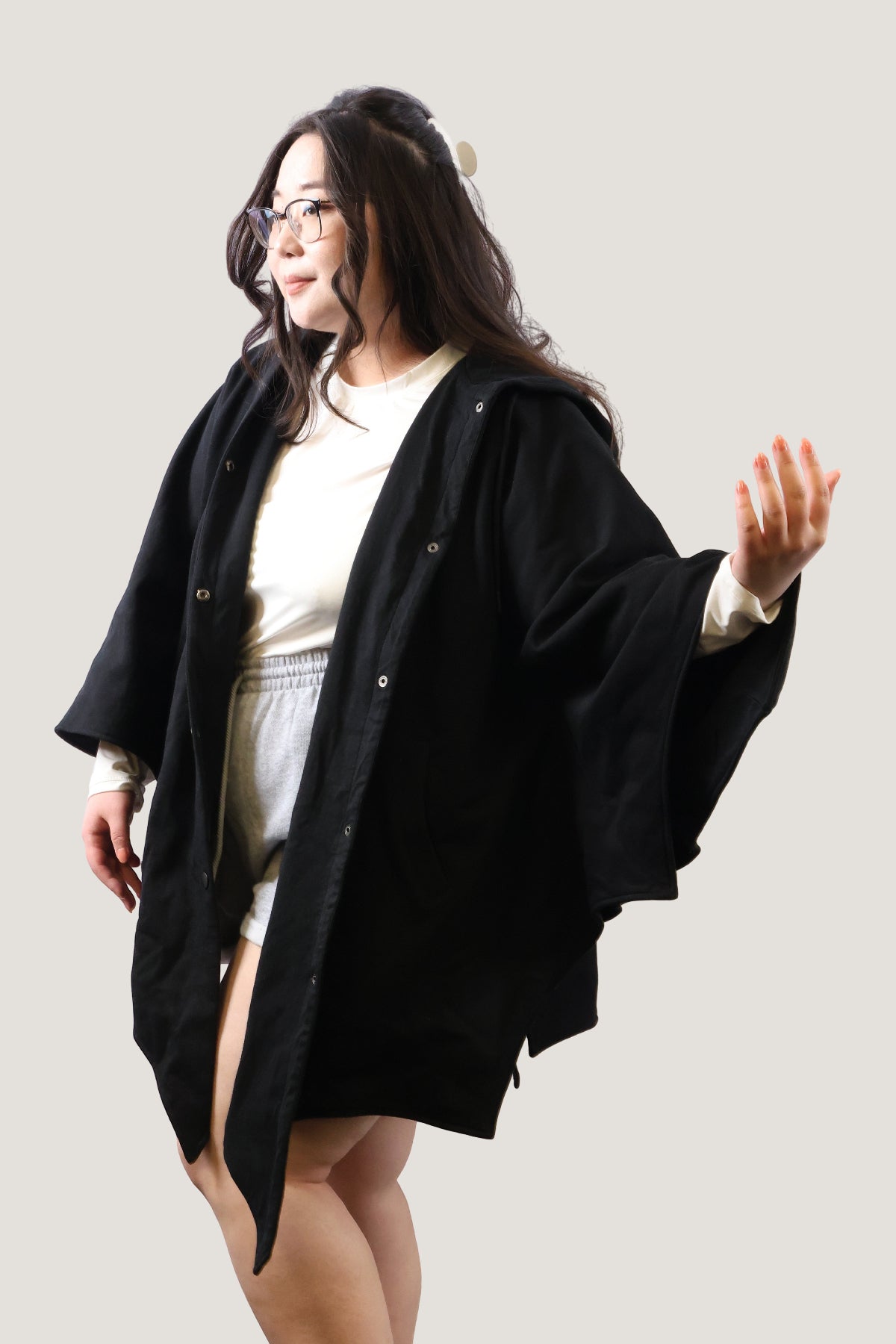 Model wearing a black bat-inspired hooded cloak from a front angled view, showing relaxed fit and draped sleeves against a light background