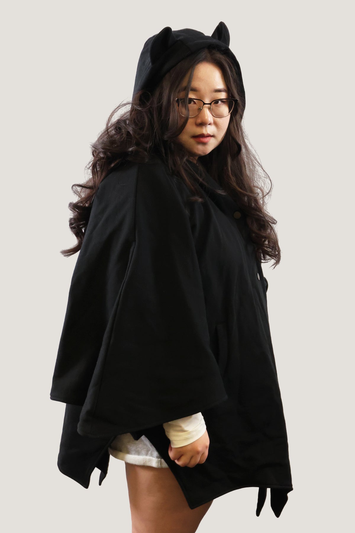 Model wearing a black bat-inspired hooded cloak with pointed ear details on the hood, showing front angled view against a light background