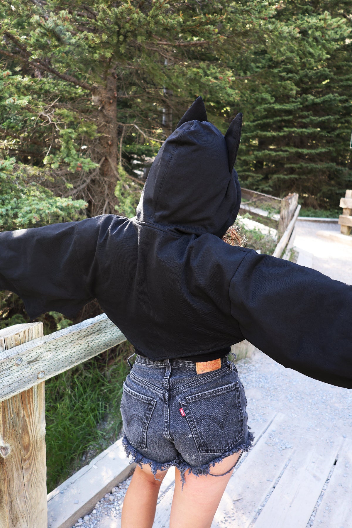 Back view of a model wearing the Nyahallo Bat Shrug with bat ears on the hood, showcasing the oversized cropped fit and hood design.