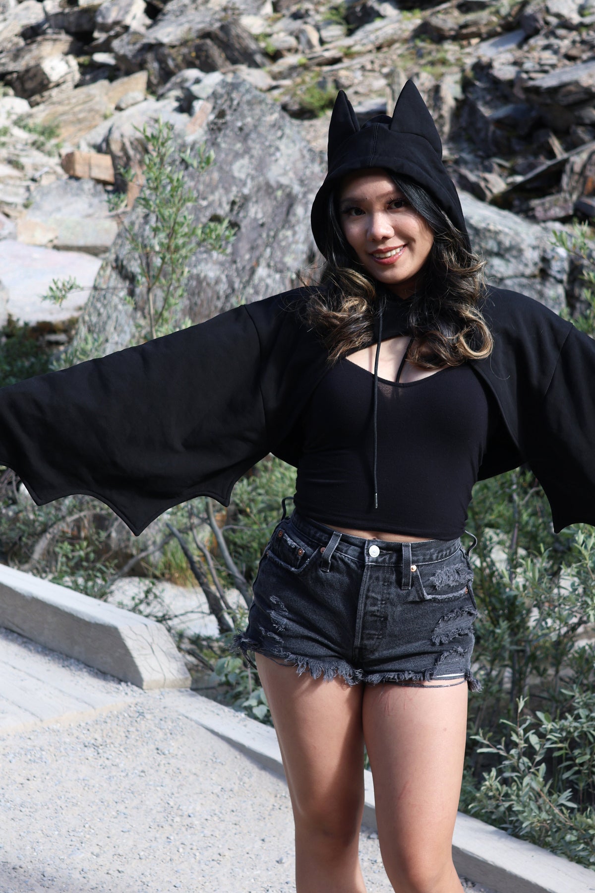 Model wearing the Nyahallo Bat Shrug with bat ears on the hood and oversized bat wing sleeves, posing with arms outstretched to showcase the wing-inspired silhouette.
