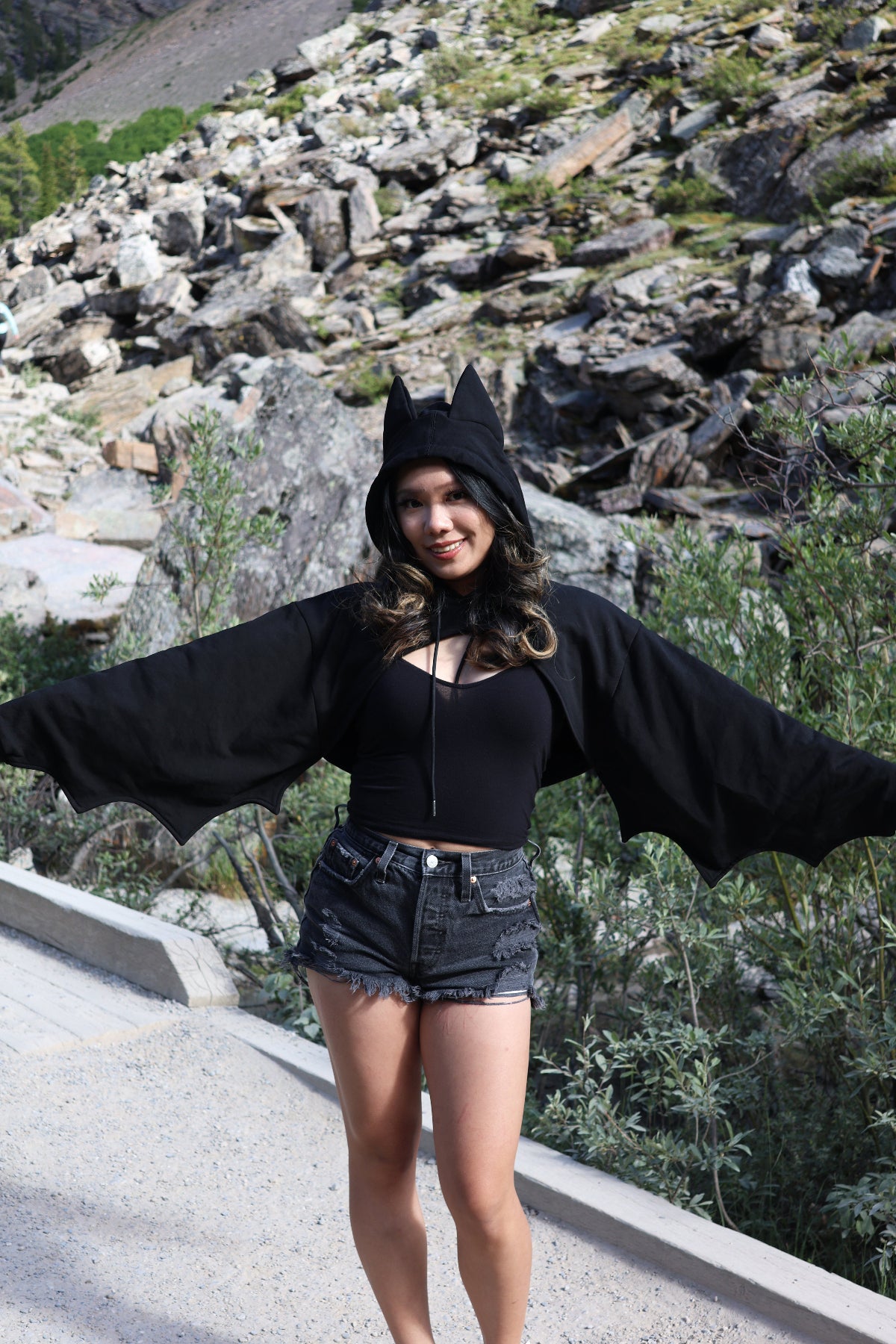 Model wearing the Nyahallo Bat Shrug with bat ears on the hood and bat wing sleeves, standing with arms outstretched to showcase the wing-inspired silhouette.