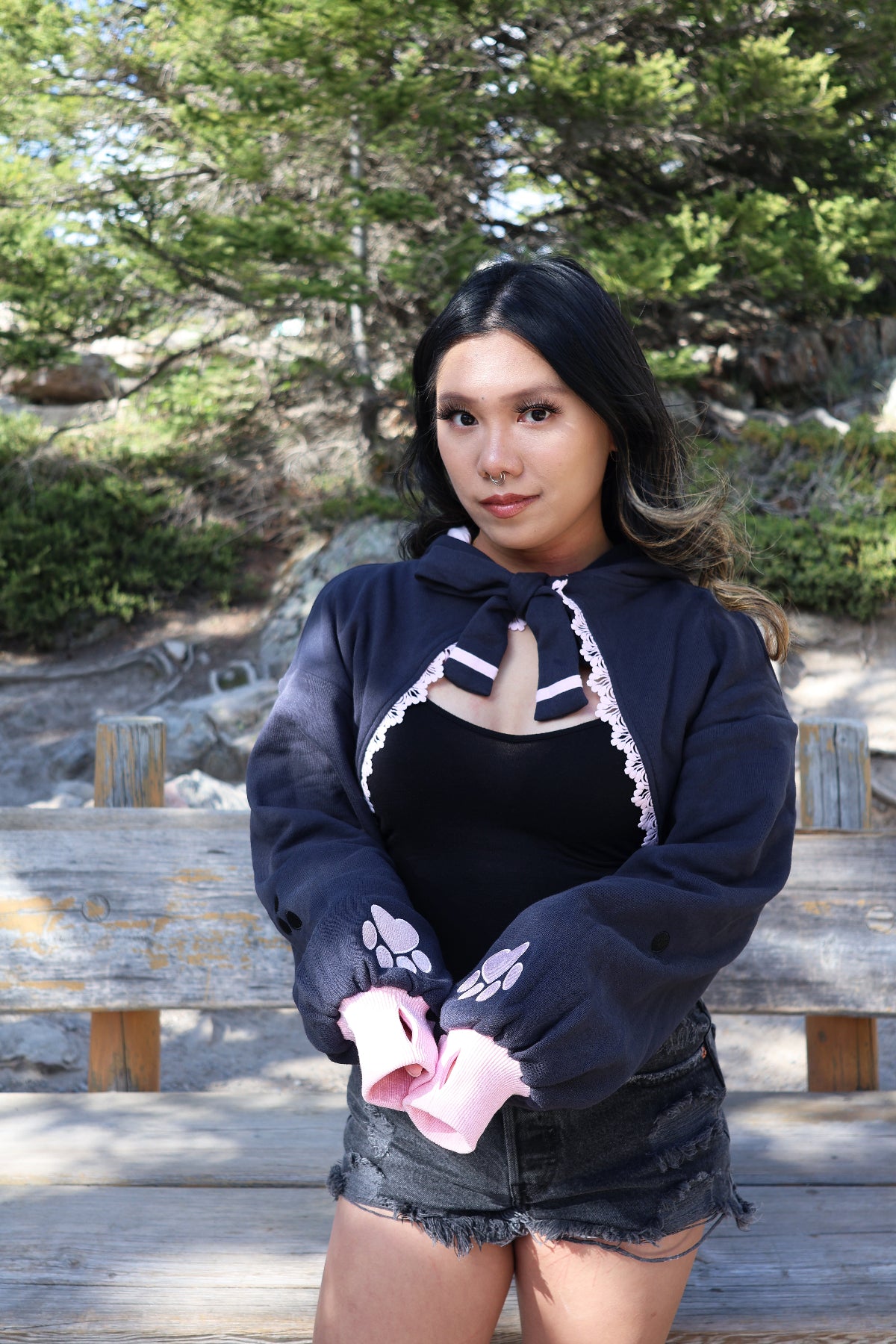 Model wearing the Nyahallo Cat Shrug with oversized sleeves, embroidered pink paw print cuffs, lace-up neckline, and hood while posing outdoors.