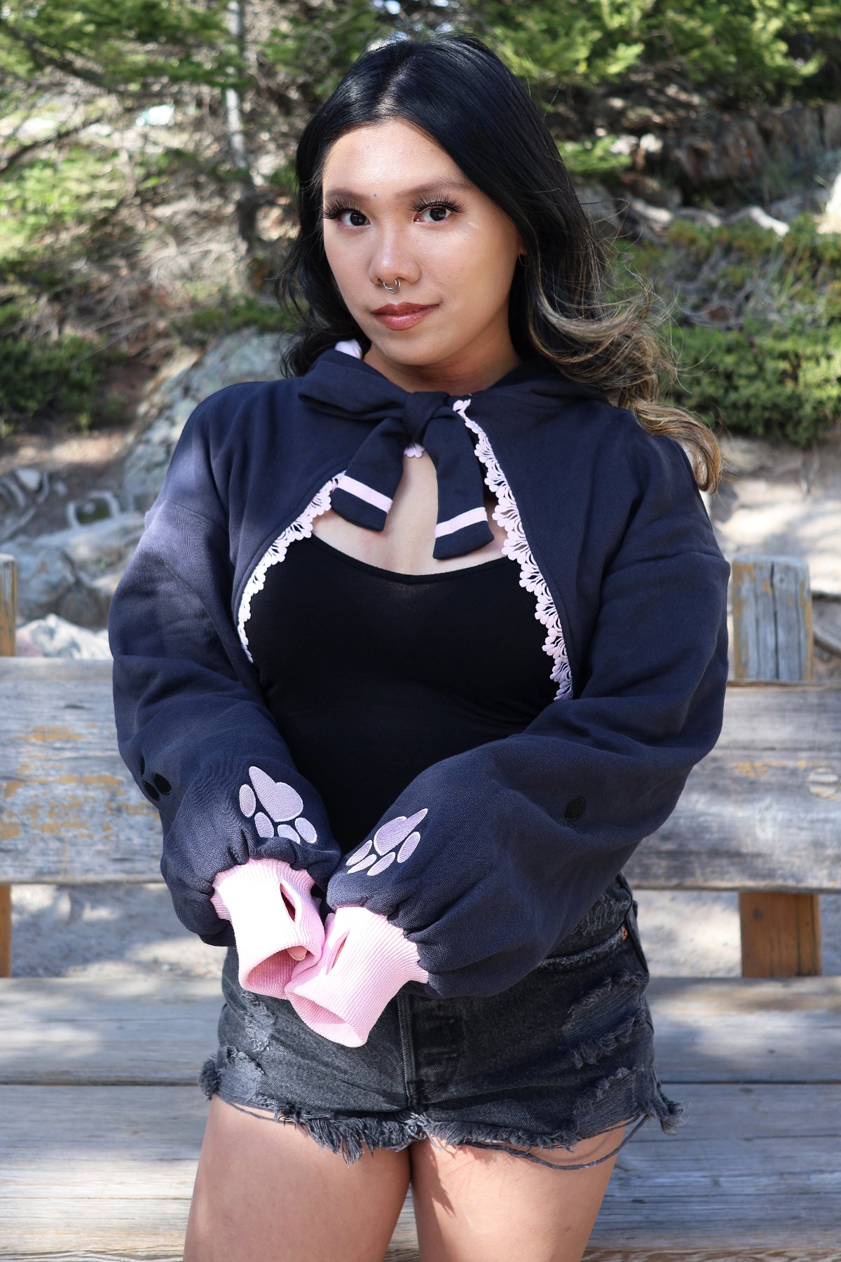 Close-up of a model wearing the Nyahallo Cat Shrug featuring oversized sleeves, embroidered pink paw print cuffs, a lace-up neckline, and pink lace trim.