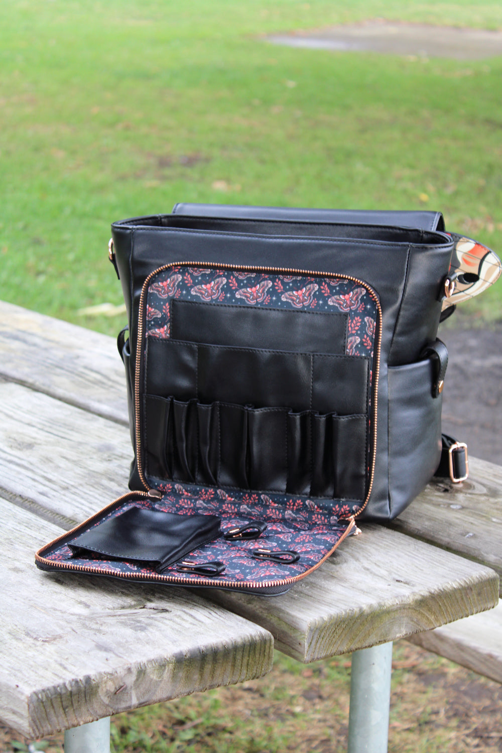 Black cecropia moth backpack opened to show interior organizer pockets and detailed botanical moth pattern lining