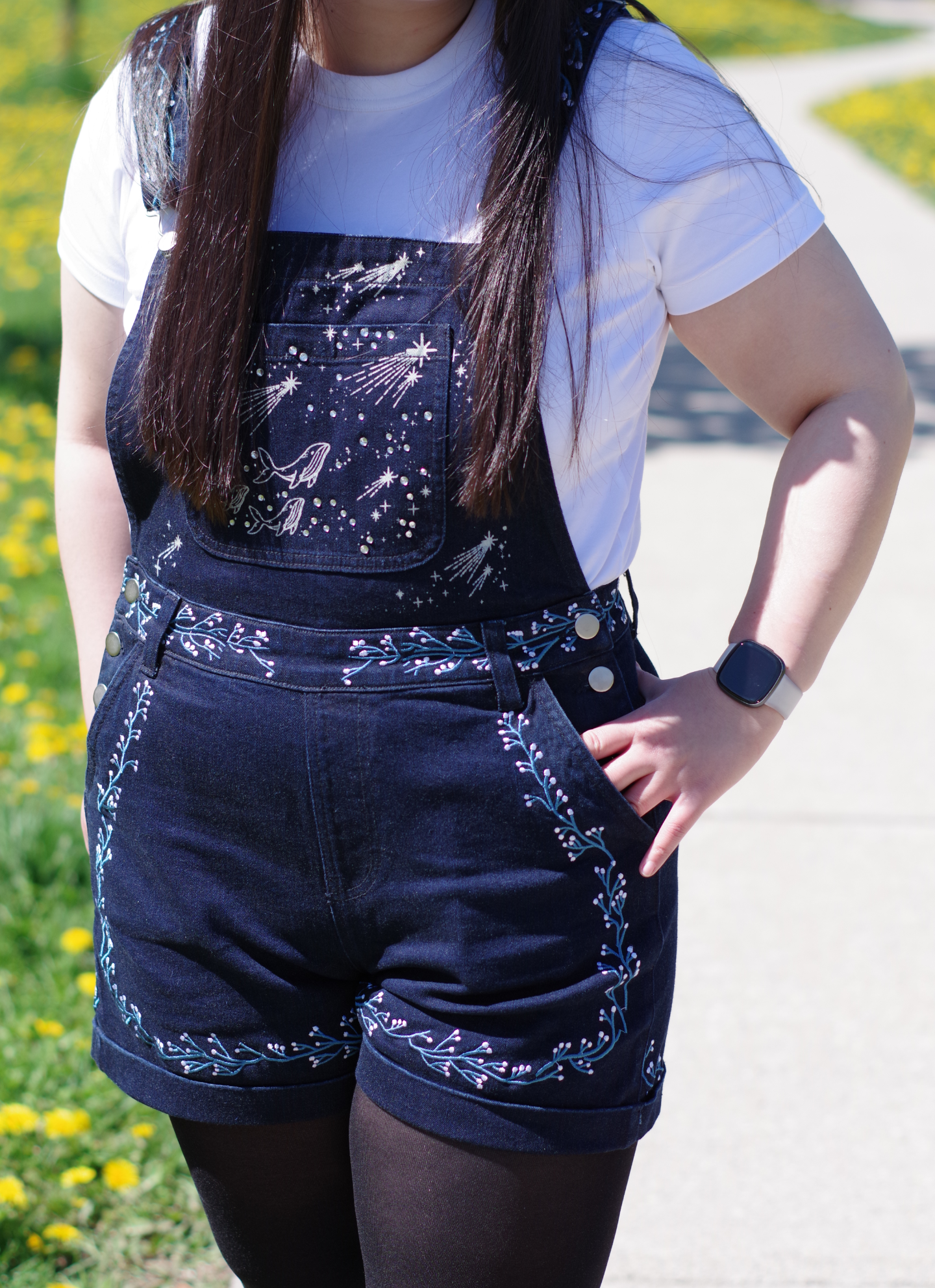 Model wearing navy celestial embroidered short overalls with constellation and shooting star details layered over a white t-shirt outdoors.