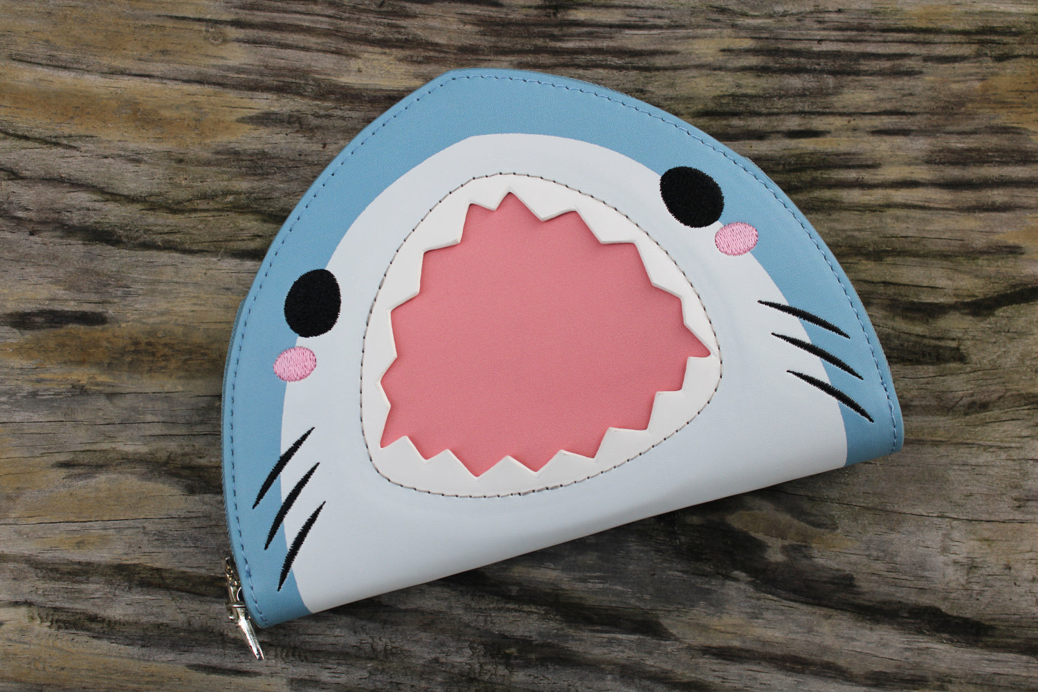 Cute shark-shaped vegan leather wallet with a playful pink mouth design resting on a rustic wooden surface.