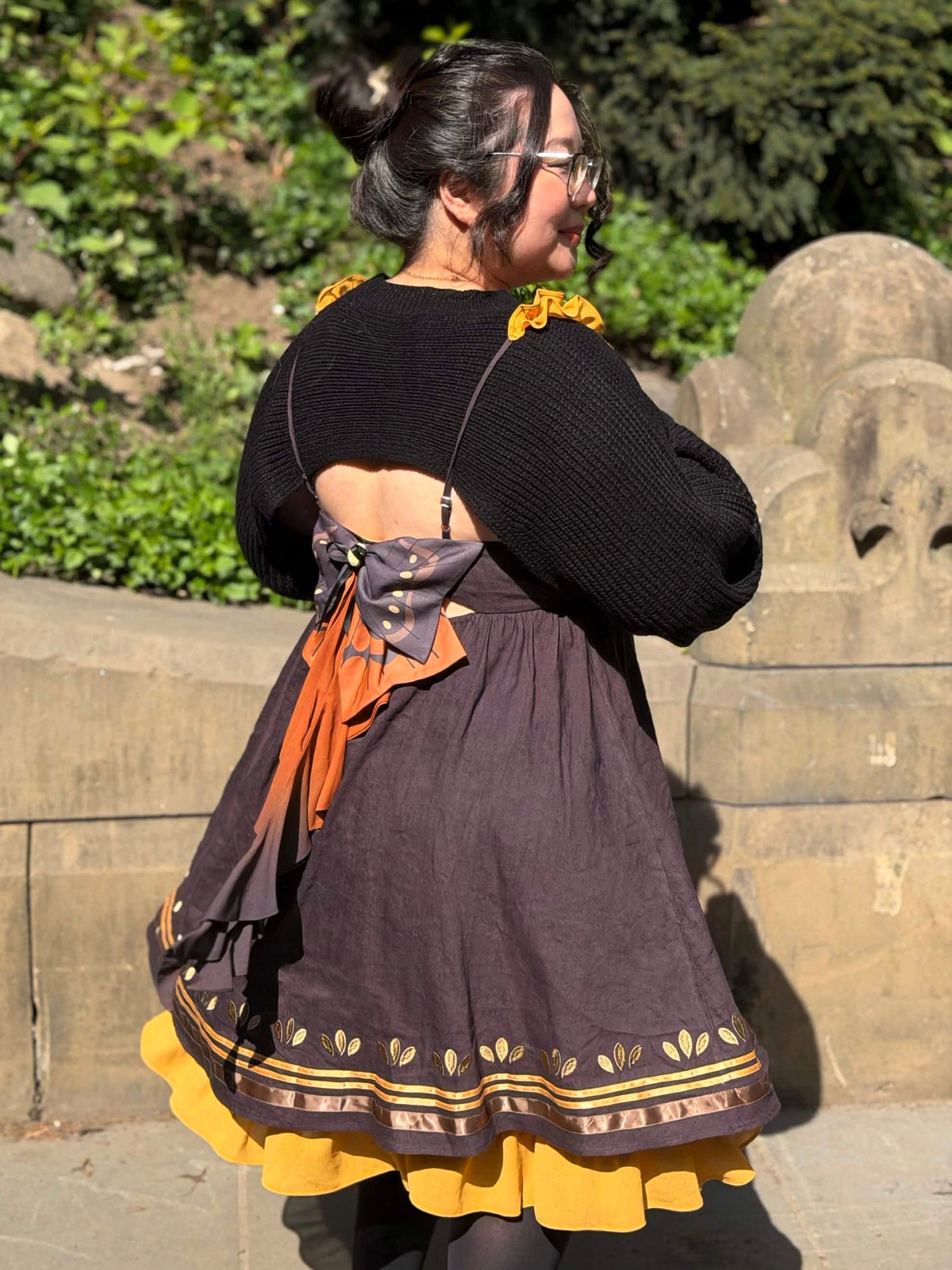 Angled back view of the Death’s-Head Hawkmoth Dress showcasing the moth wing bow detail, flowing ribbon tails, and layered golden hem outdoors in sunlight.