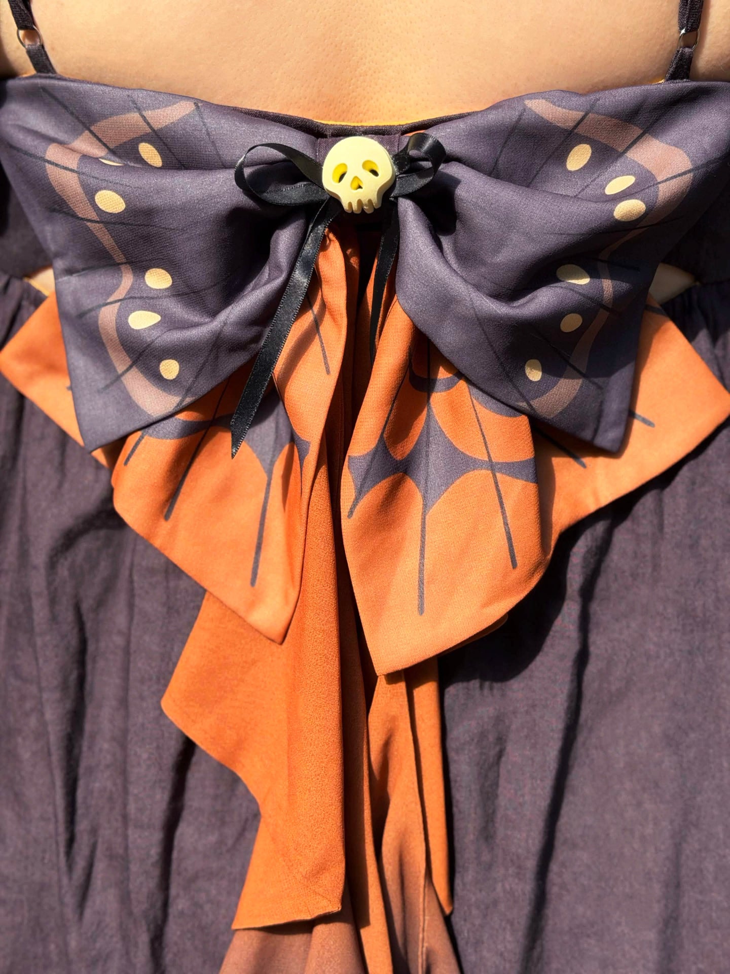 Close-up detail of the Death’s-Head Hawkmoth Dress featuring a moth wing bow, layered orange ribbons, and a small skull charm accent.