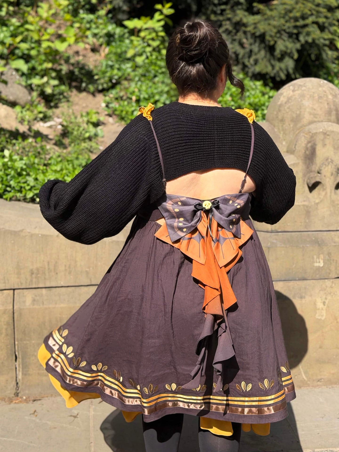 Centered back view of the Death’s-Head Hawkmoth Dress featuring moth wing-inspired bow details, layered ribbon tails, and flowing golden ruffles in warm sunlight.