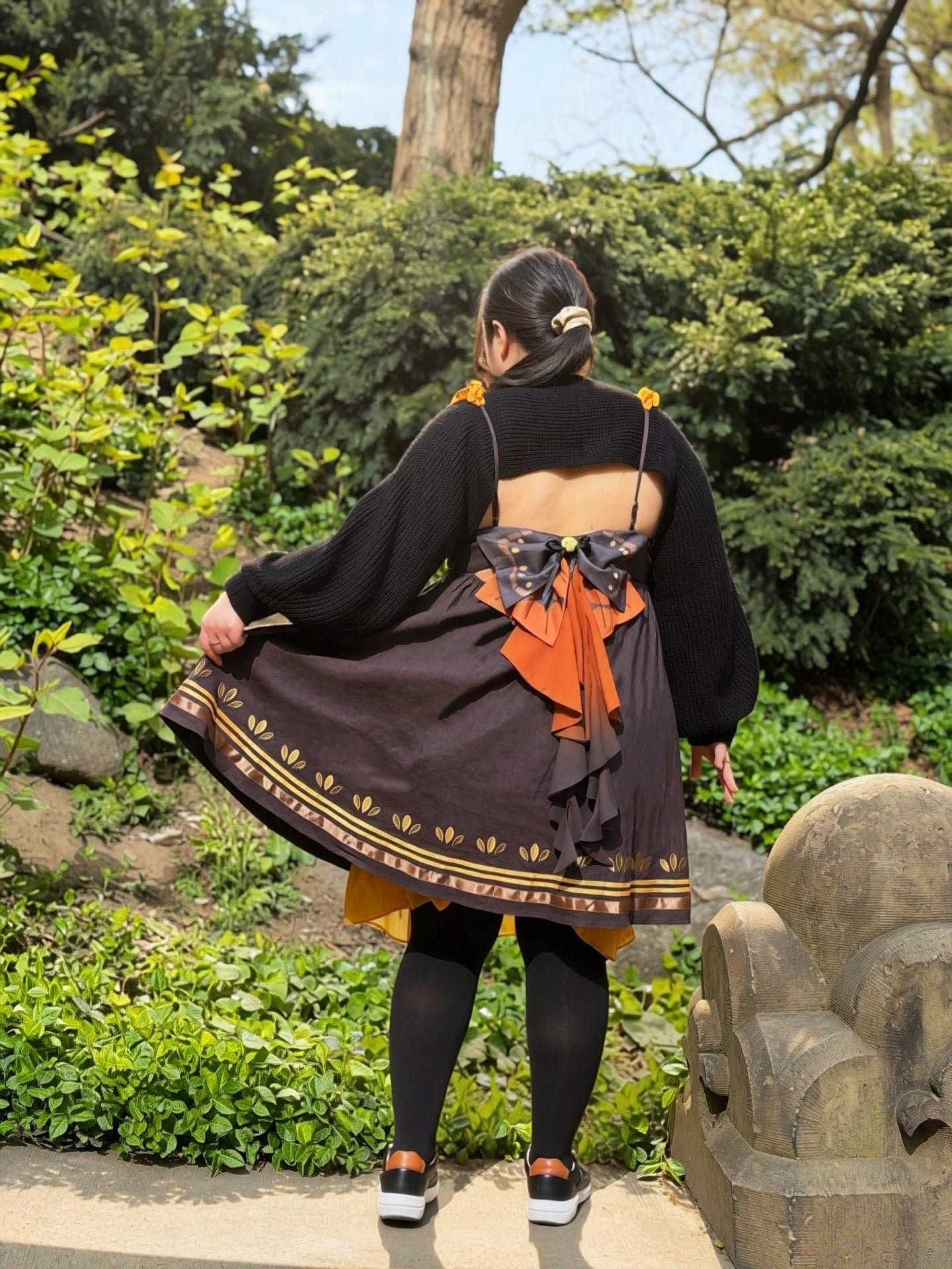 Editorial back view of the Death’s-Head Hawkmoth Dress featuring layered moth-inspired bows, ribbon tails, and gold trim details in a lush garden setting.