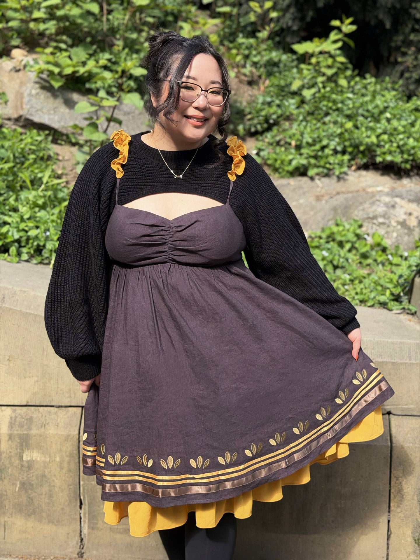 Model wearing the Death’s-Head Hawkmoth Dress with black knit shrug sleeves and yellow ruffle details in a sunlit garden.