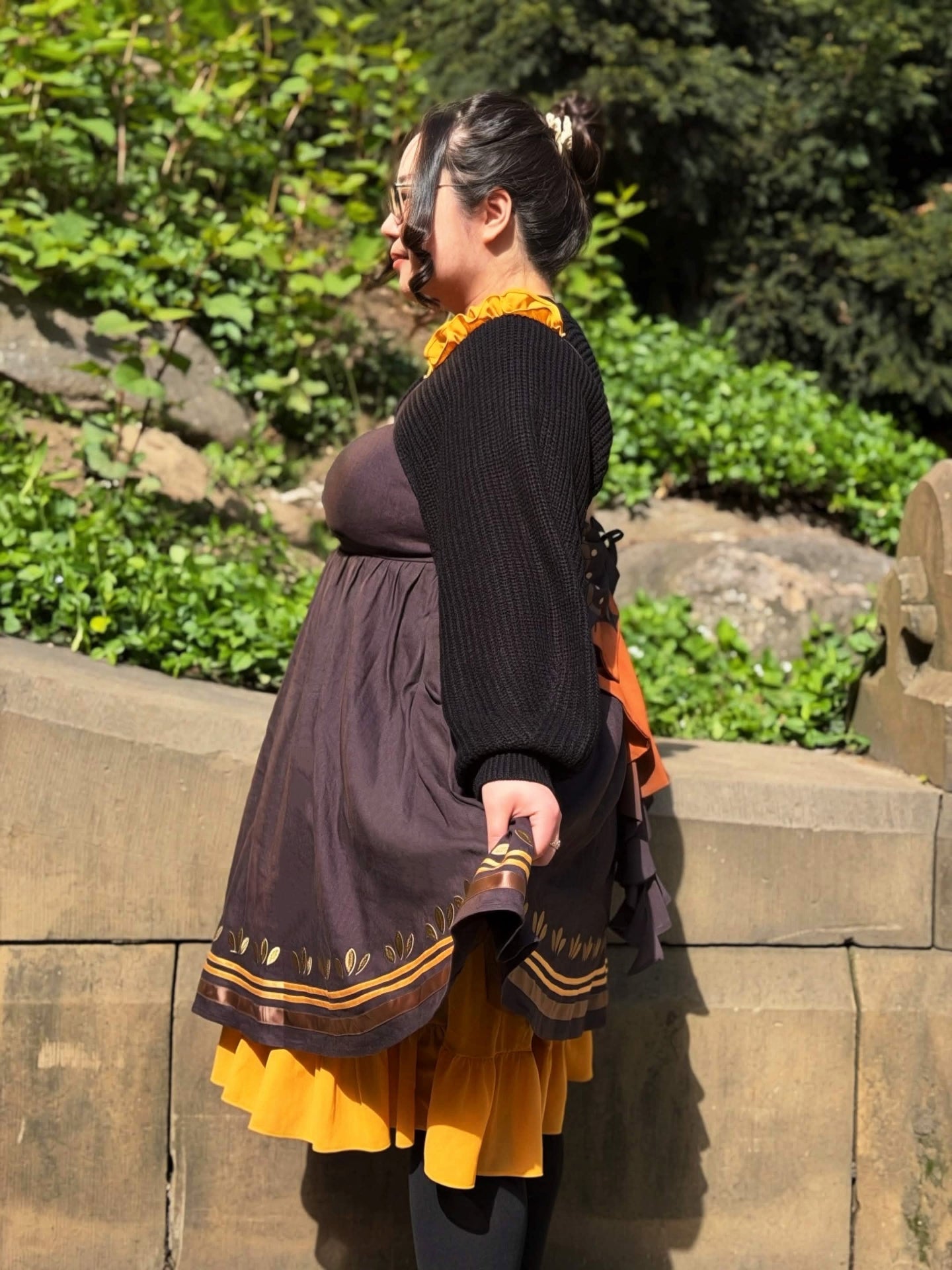 Side profile view of the Death’s-Head Hawkmoth Dress with flowing golden underskirt, textured black shrug sleeves, and moth-inspired detailing in a garden setting.