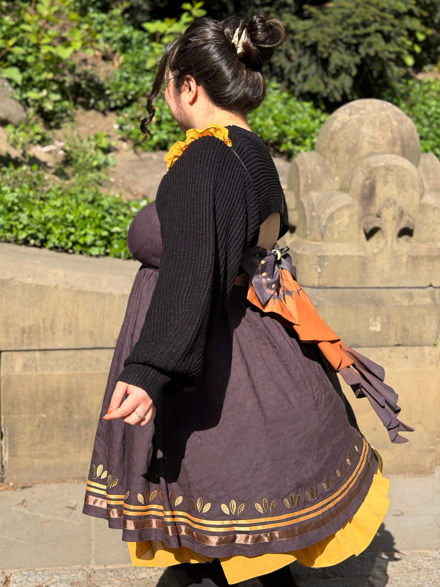 Side twirl view of the Death’s-Head Hawkmoth Dress featuring flowing ribbon tails, moth wing-inspired bow details, and layered golden ruffles in warm sunlight.