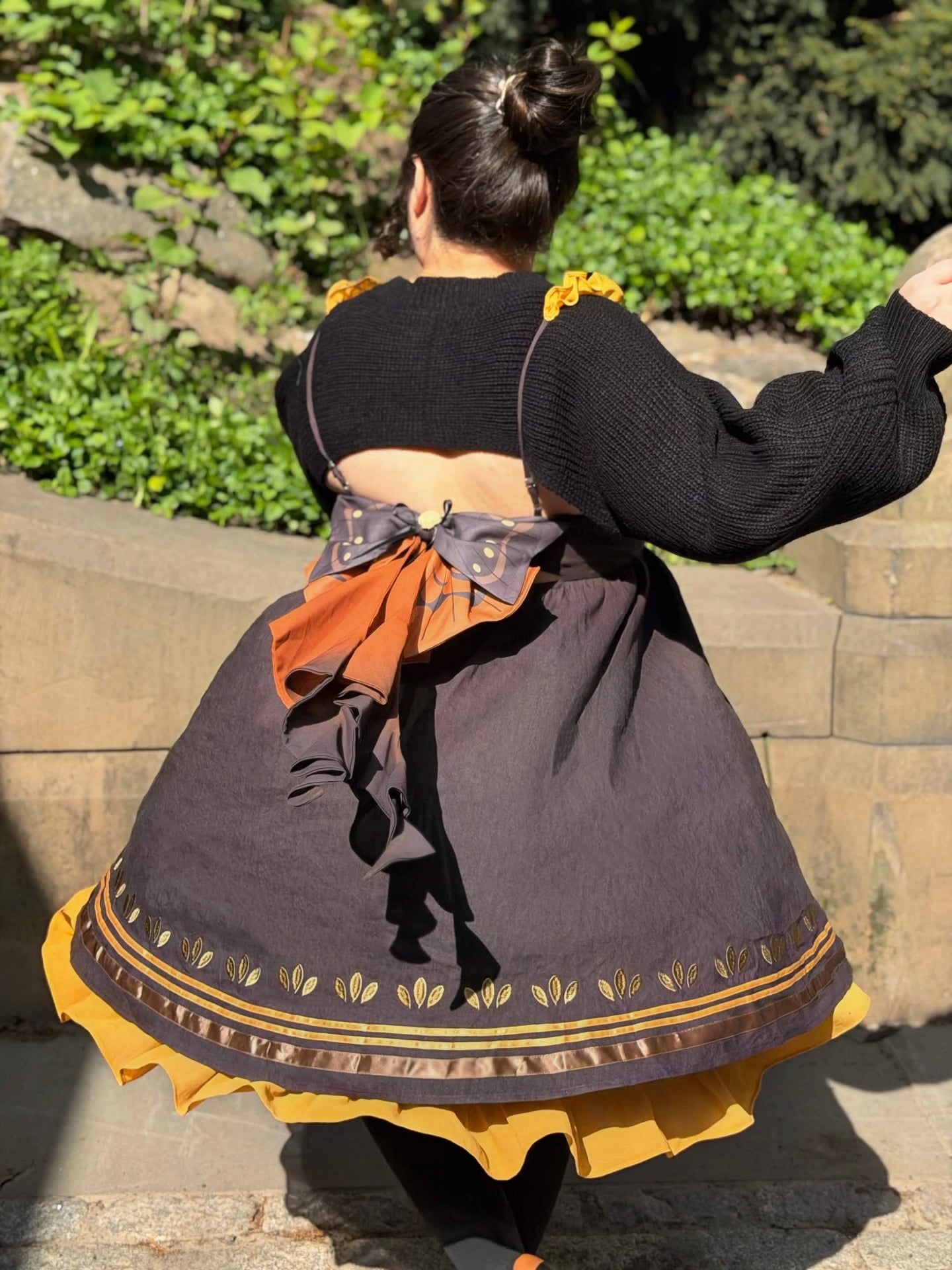 Back twirl view of the Death’s-Head Hawkmoth Dress featuring layered moth wing bows, flowing ribbon tails, and golden ruffle trim in warm sunlight.