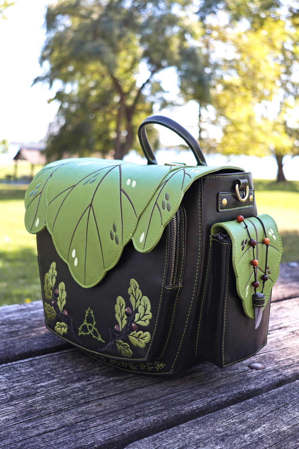 Green and dark brown handbag with leaf design on a wooden surface outdoors