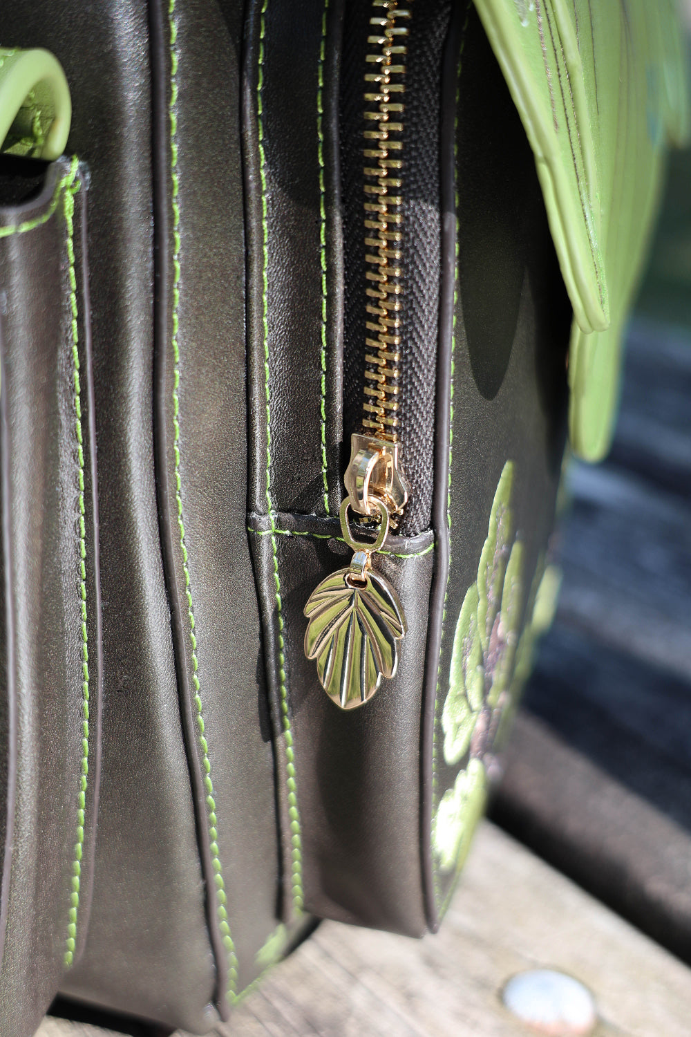 Close-up of a green leaf-shaped zipper pull on a dark brown bag with leaf patterns.