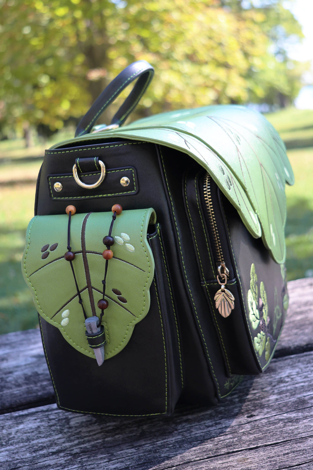Dark brown backpack with green leaf design on a wooden surface