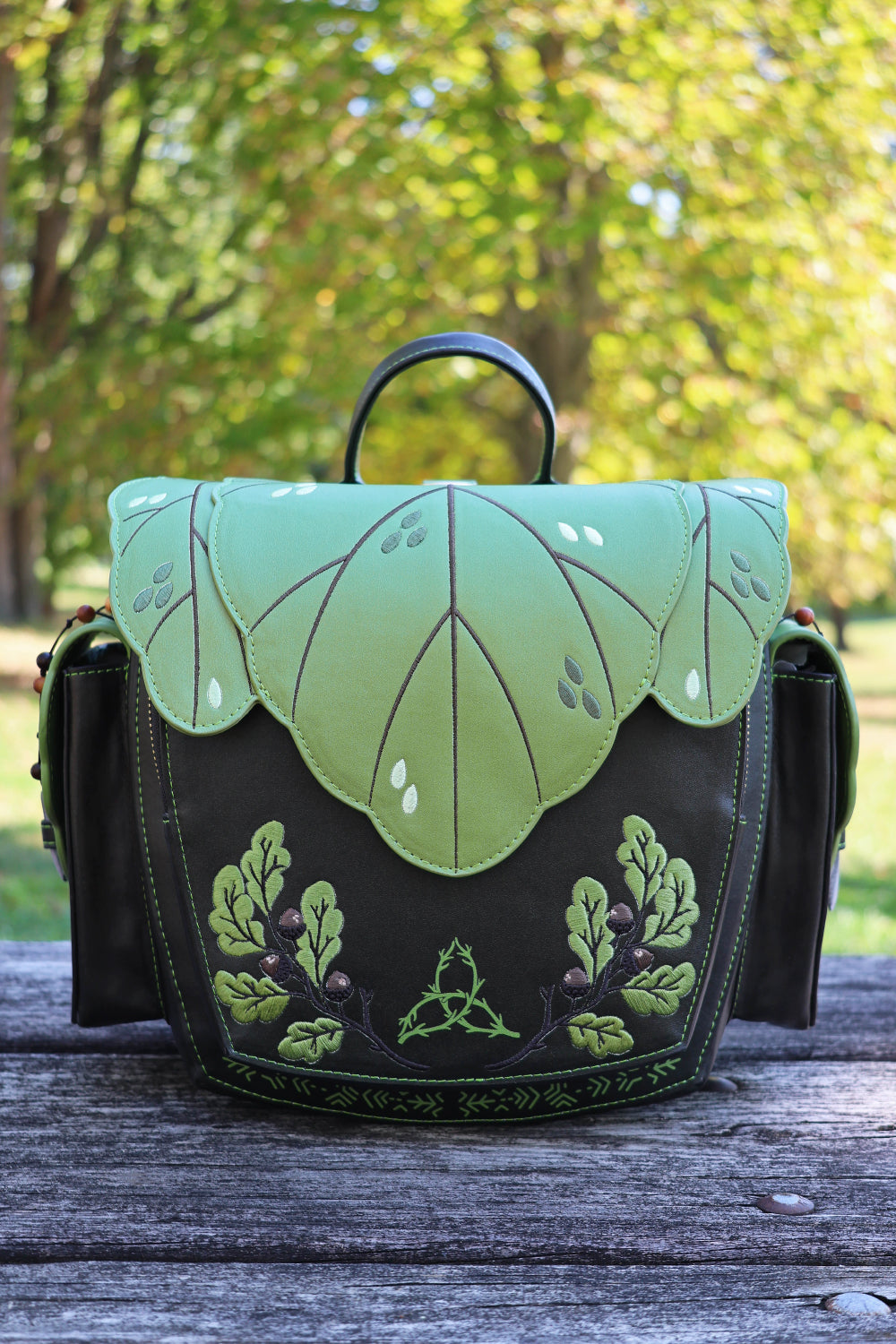 Dark brown and green leaf-patterned bag on a wooden surface with a blurred natural background