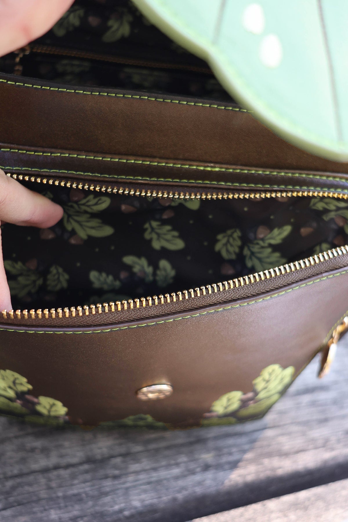 Close-up of the open Druid backpack showing the botanical leaf-print interior lining, zippered compartments, gold hardware, and green contrast stitching.