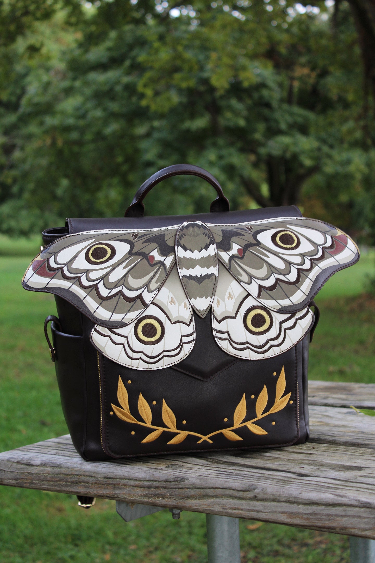 Black emperor moth backpack with whimsical fairycore, forestcore, and entomology fashion inspired design displayed outdoors