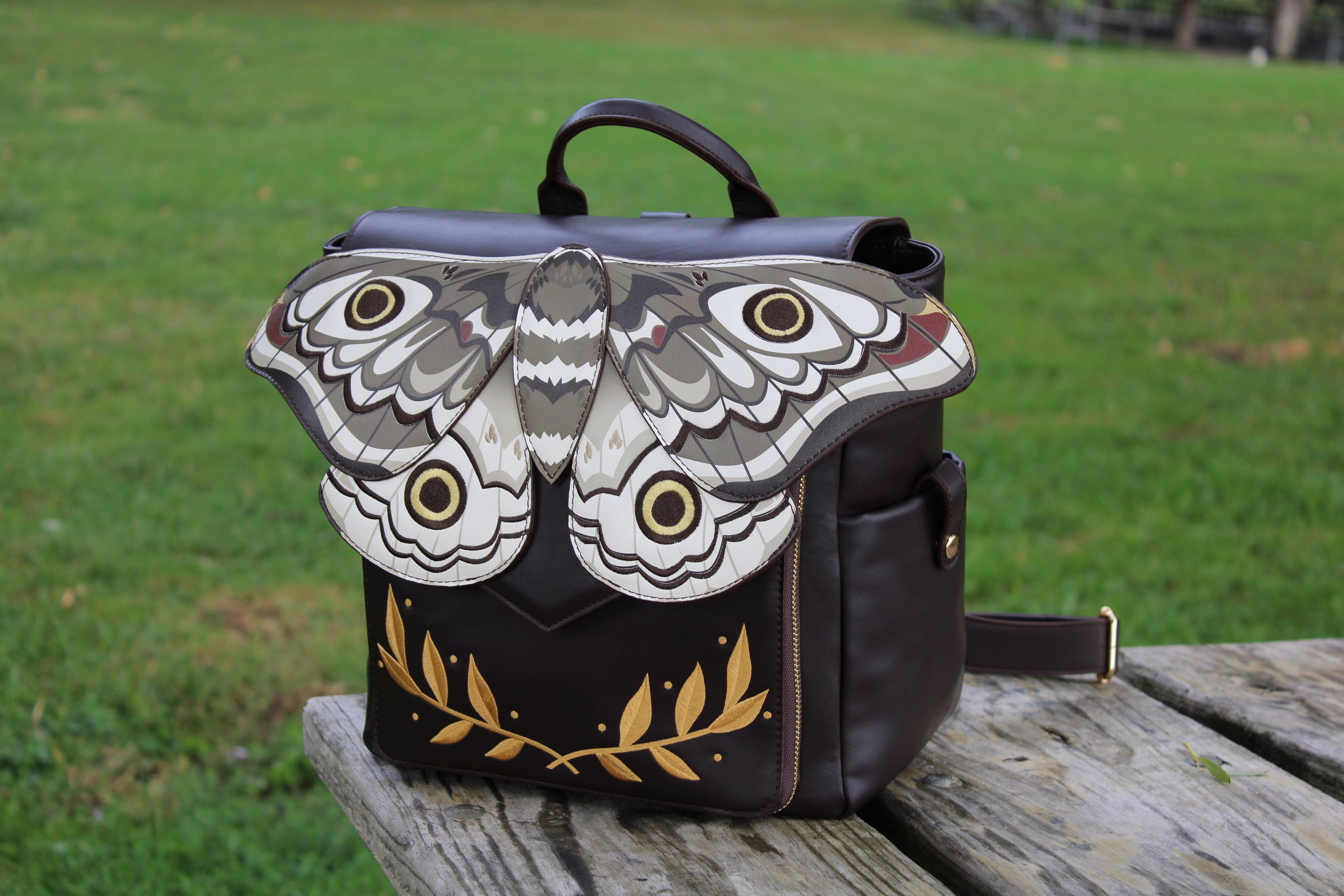 Front view of the Emperor Moth Backpack featuring layered moth wings, embroidered eye spots, gold botanical accents, and a whimsical fantasy-inspired design.