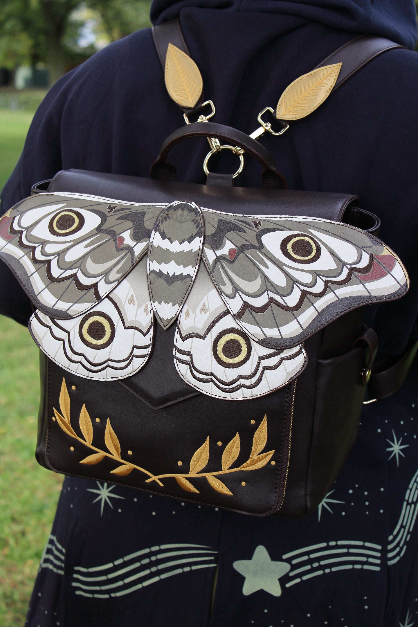 Close-up of the Emperor Moth Backpack featuring sculpted moth wings, embroidered eye spots, gold leaf embroidery, and adjustable leaf-shaped shoulder straps.