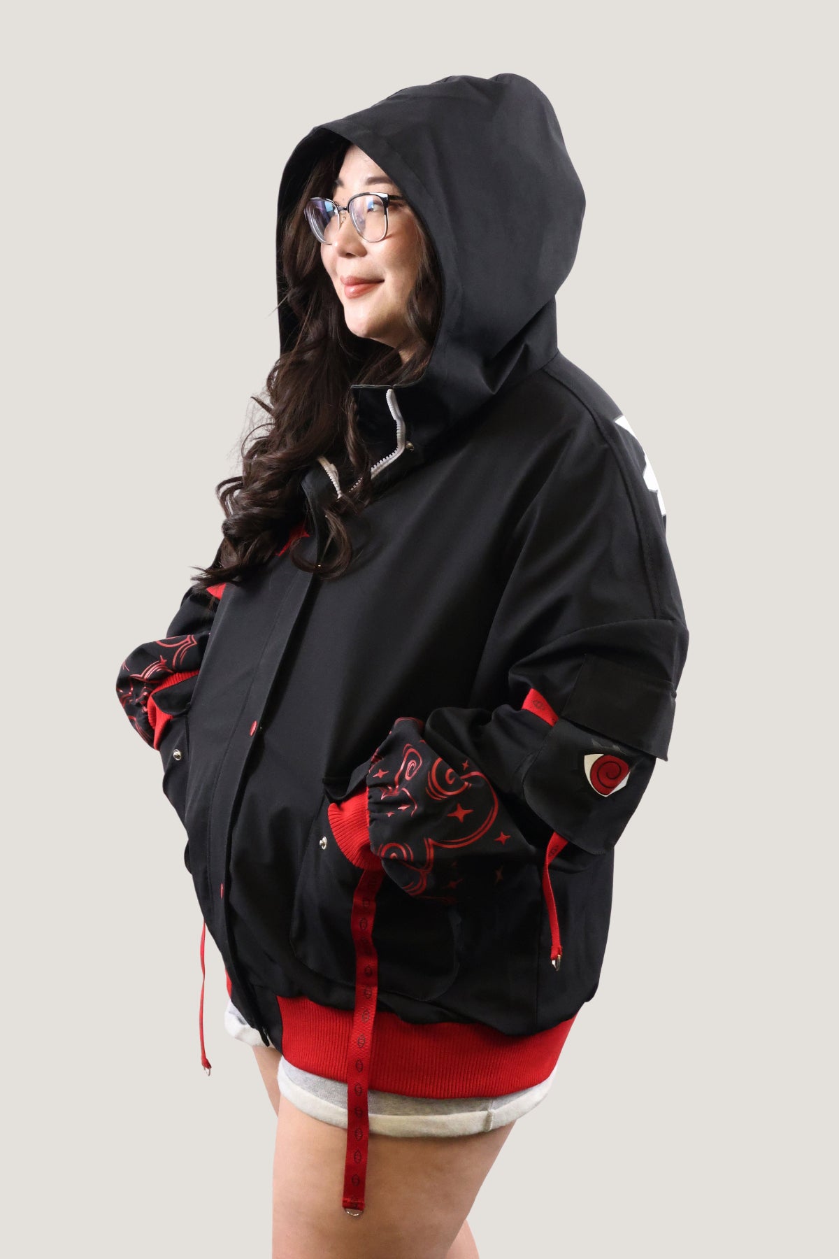 Side view of a model wearing the black and red Fallen Angel bomber jacket with the hood up, showcasing the red pattern details on the oversized sleeves.