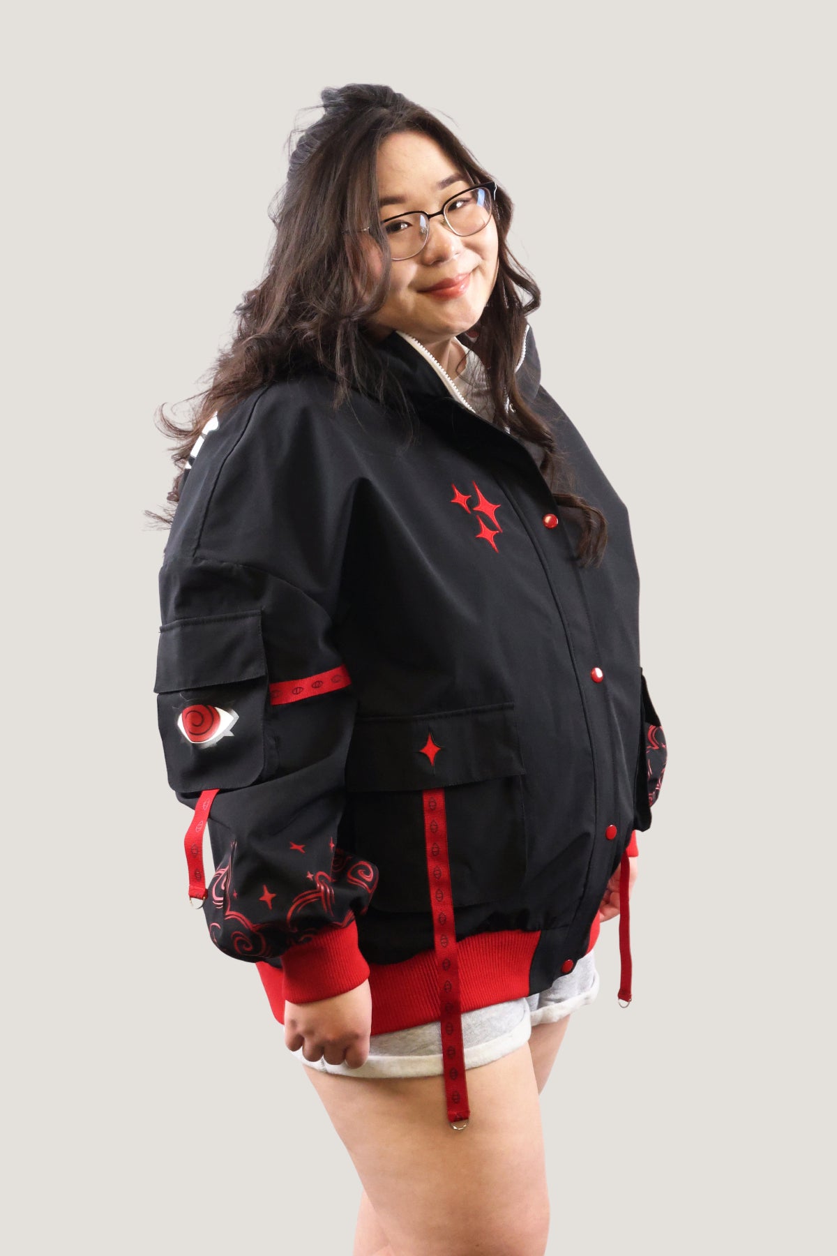 Front view of the Fallen Angel bomber jacket featuring red utility straps, embroidered sleeve patches, and red star details on a black canvas background.