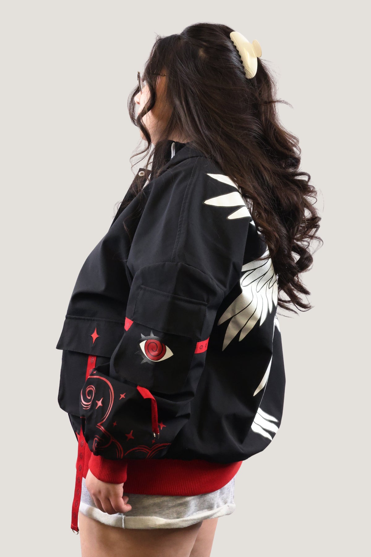 Side view of the Fallen Angel jacket showing white wing embroidery on the shoulder and a red eye patch on the black cargo sleeve pocket.