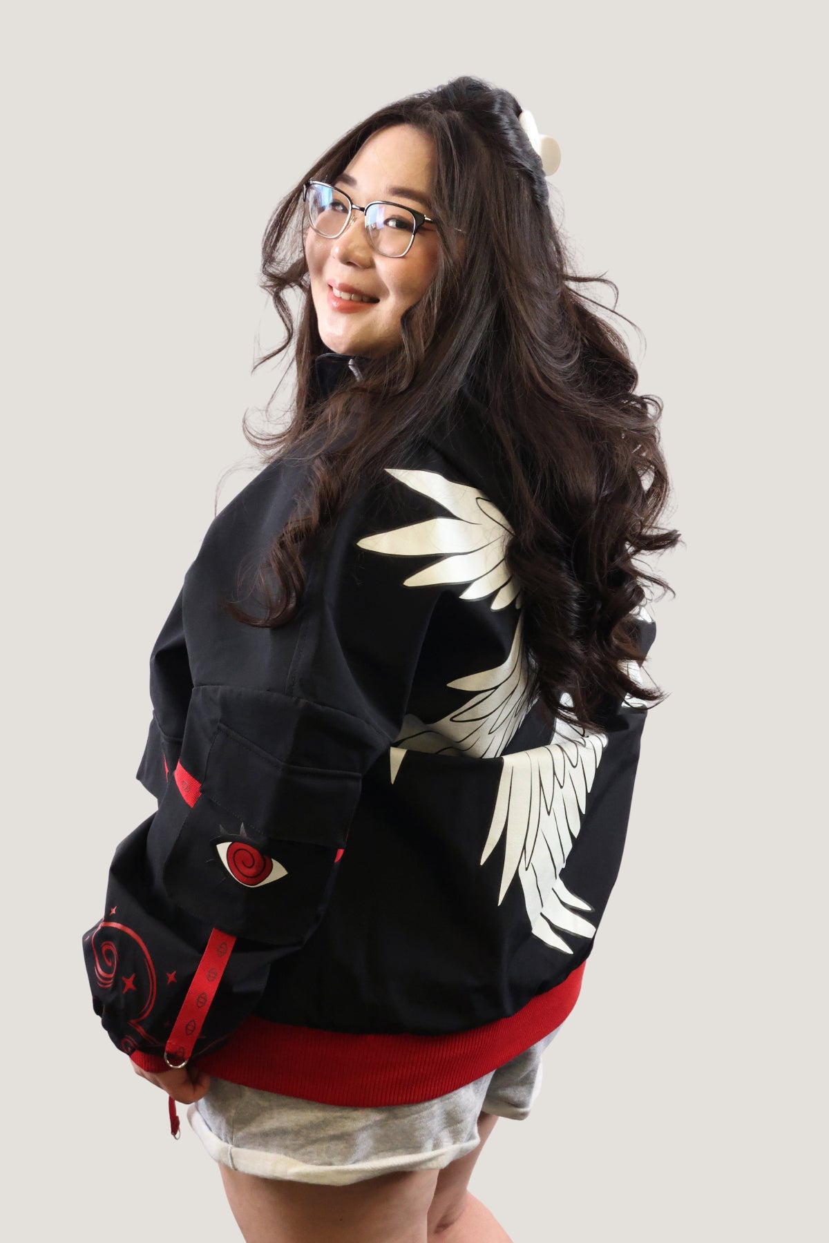 A model wearing the Fallen Angel Jacket with white wing embroidery on the back, sitting on a concrete ledge in an urban setting.