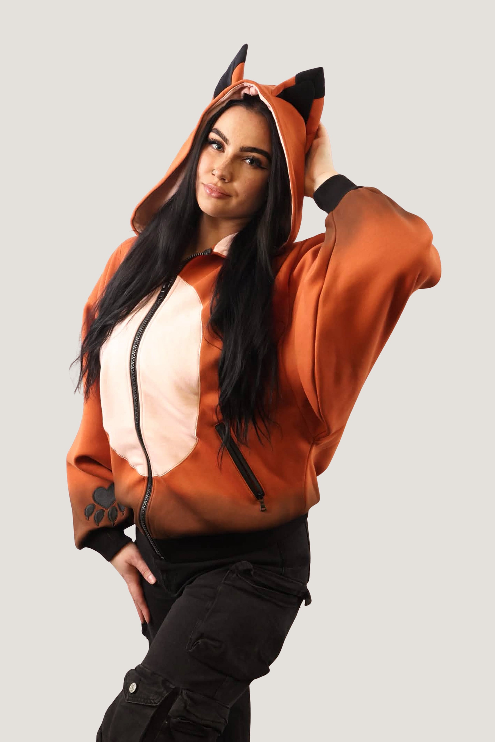 A model wearing an orange and cream Fox Hooded Sweatshirt with pointed animal ears on the hood, posing against a neutral background.