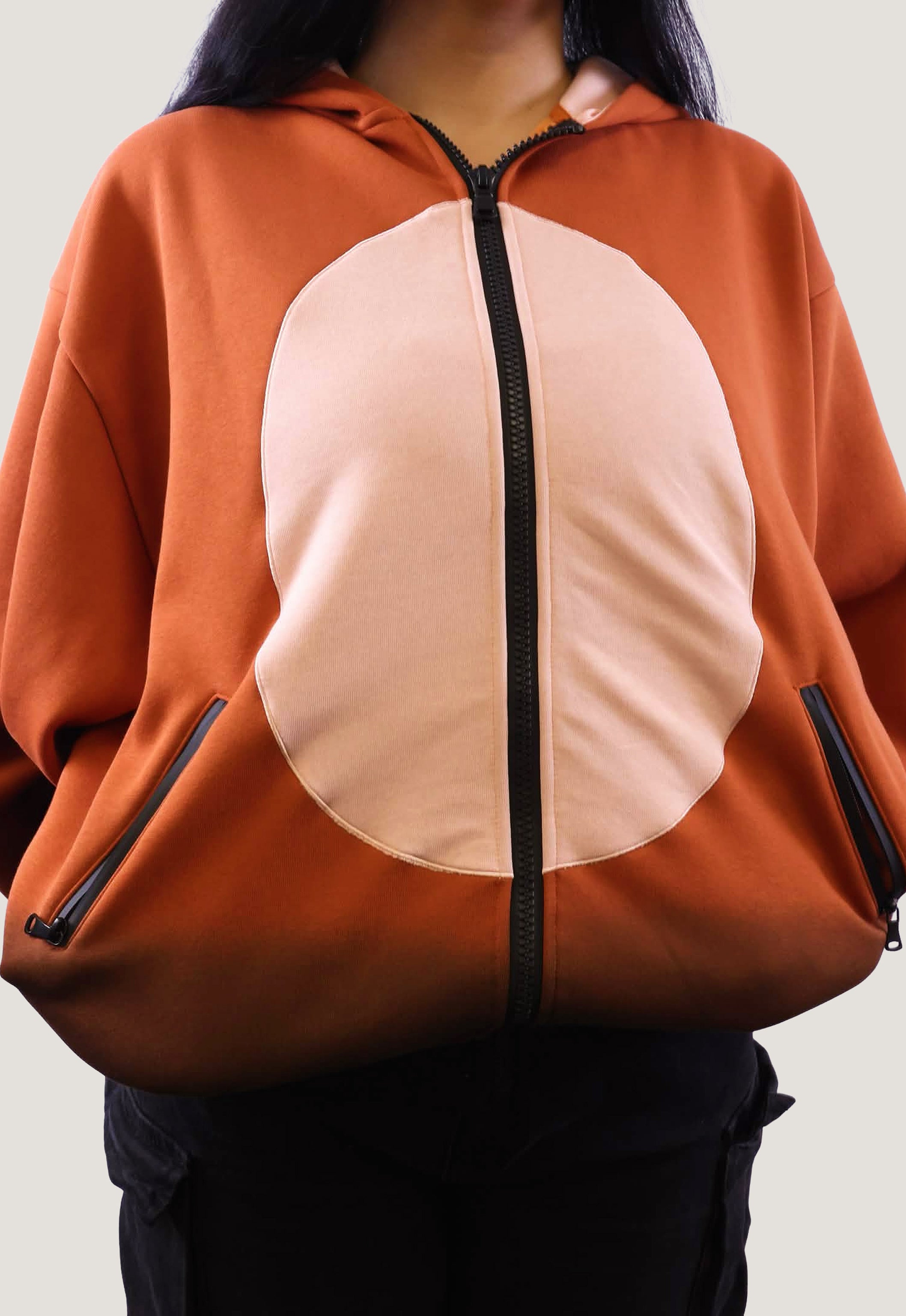 Close-up shot of the Fox Hooded Sweatshirt showing the cream circular belly panel, black zipper, and side pockets on the orange fleece fabric.
