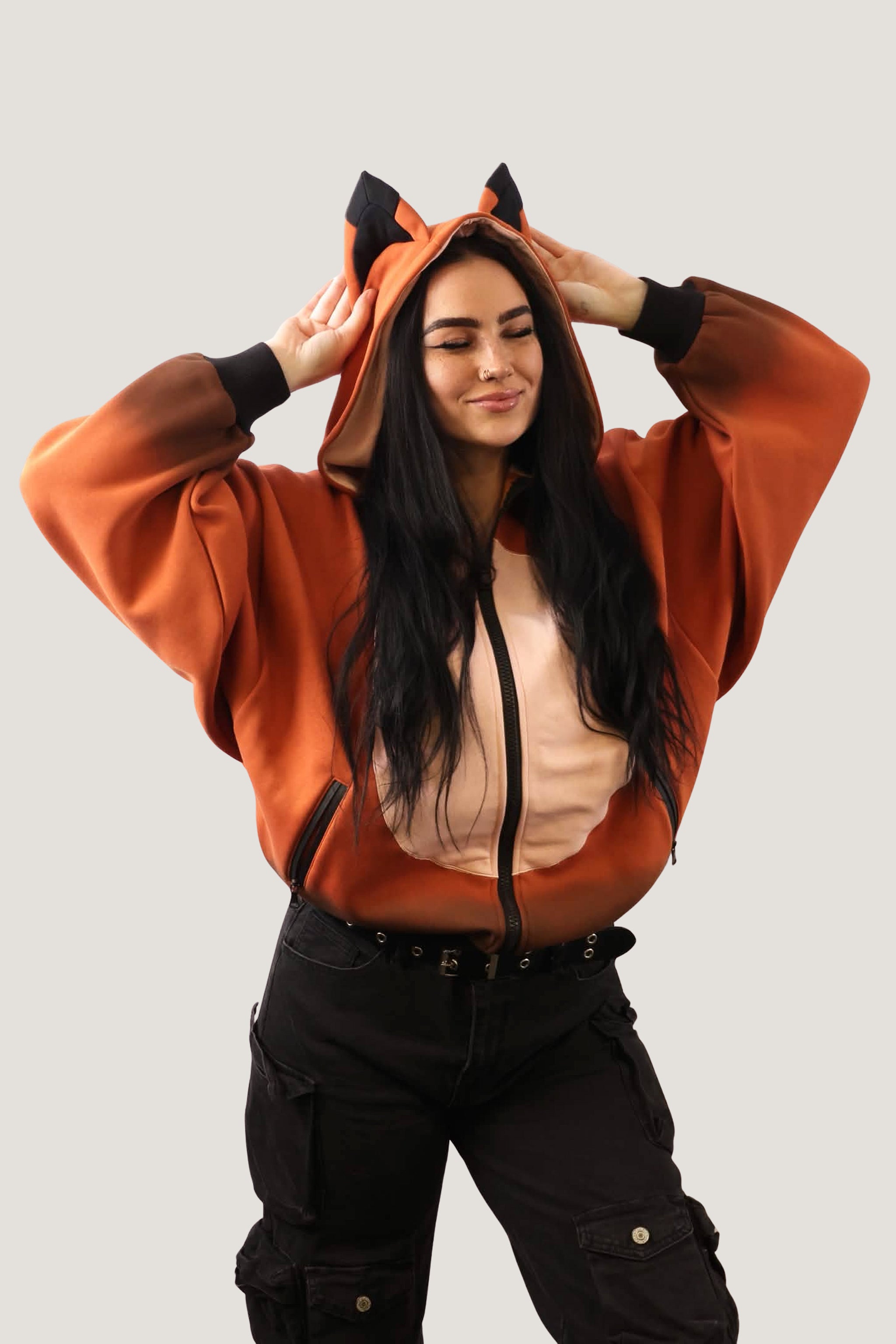 A model with hands on the hood of an orange Fox Hooded Sweatshirt, showcasing the black animal ear details and the contrasting cream belly panel.