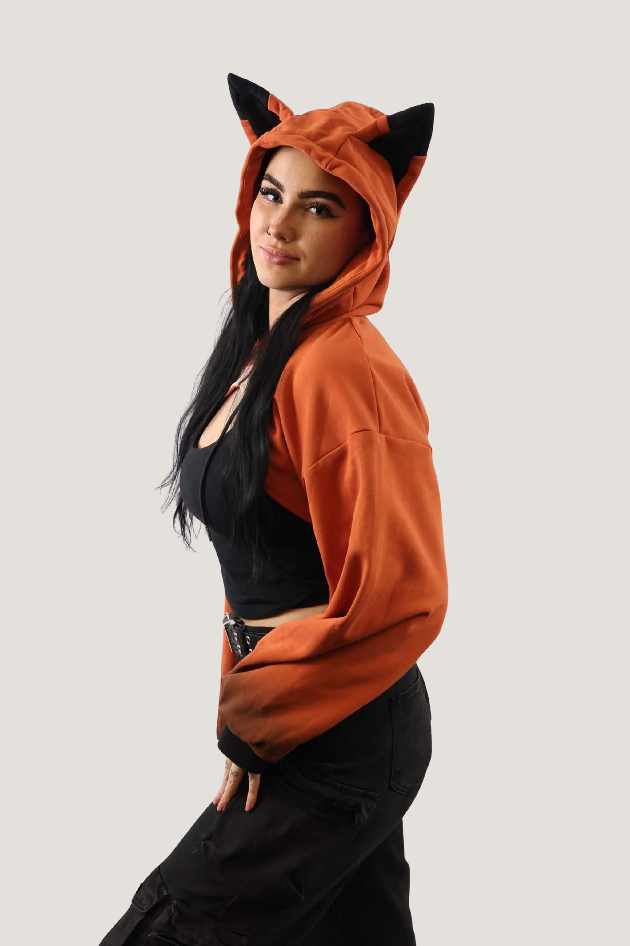 Side angled view of an orange fox hooded shrug with black ears, highlighting the cropped silhouette and playful hood design