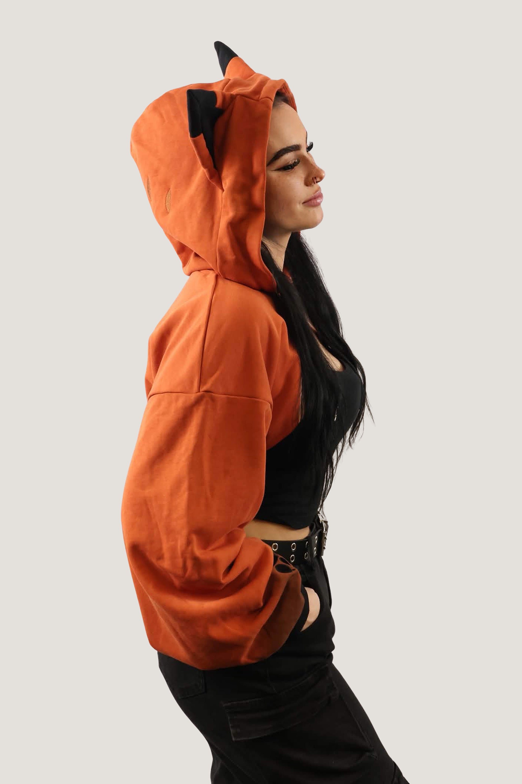 Side profile of model wearing an orange fox-inspired hooded shrug with black ear details, showing cropped fit and relaxed sleeves against a light background