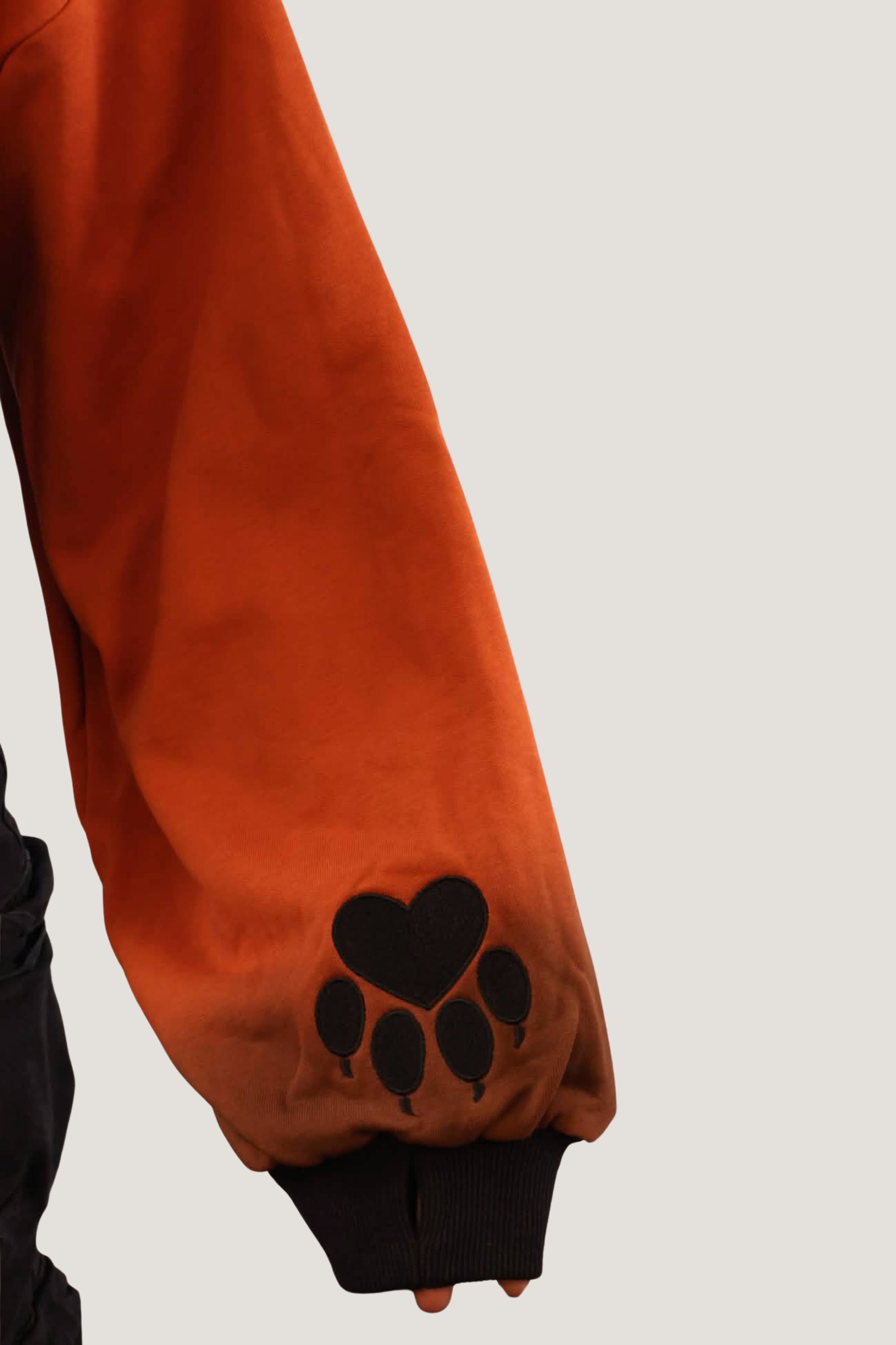 Close-up of orange fox-inspired shrug sleeve with black paw print detail and ribbed cuff against a light background