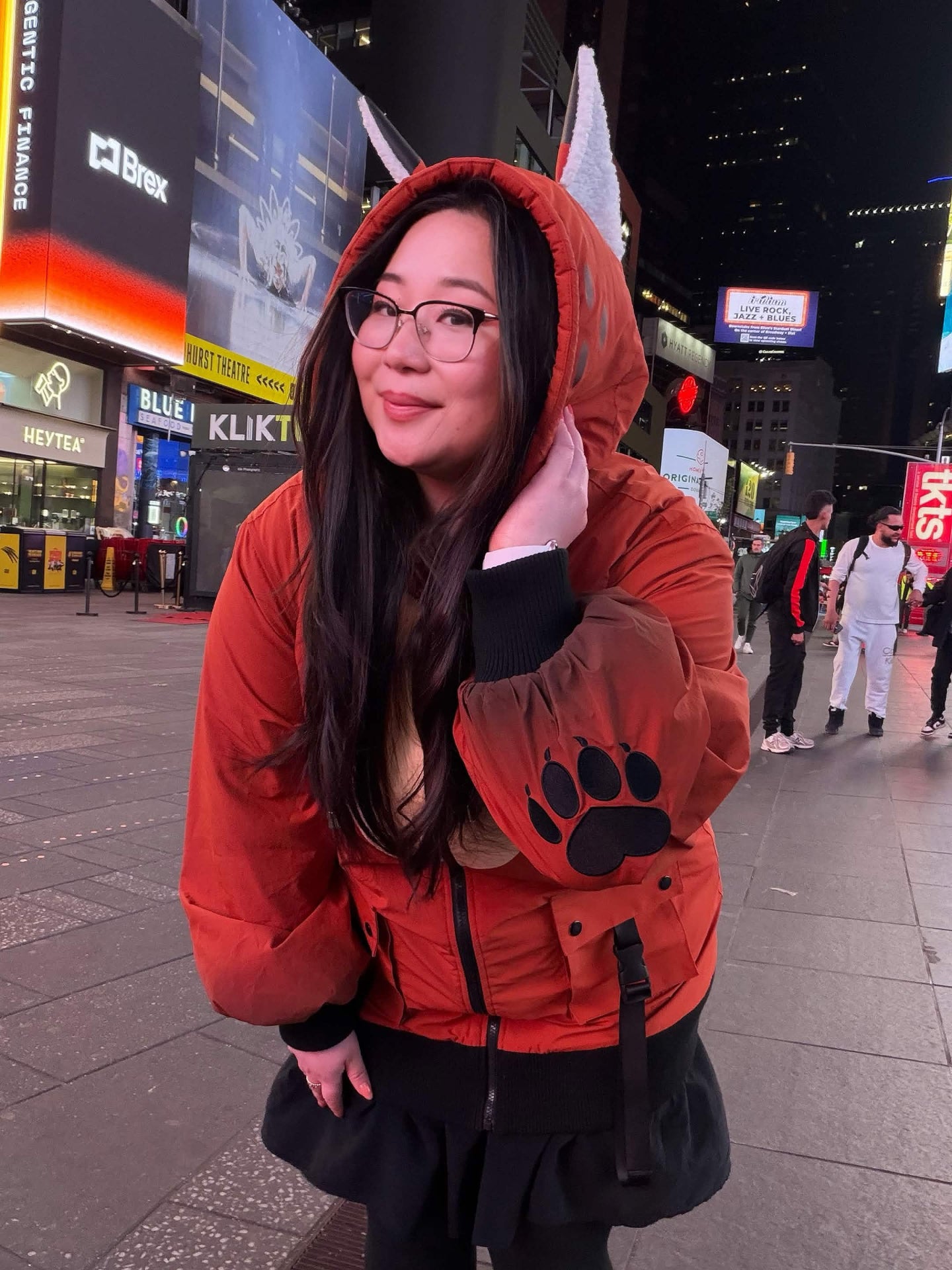 Model wearing a whimsical fox-inspired jacket with fox ears and paw print sleeve details in Times Square at night.