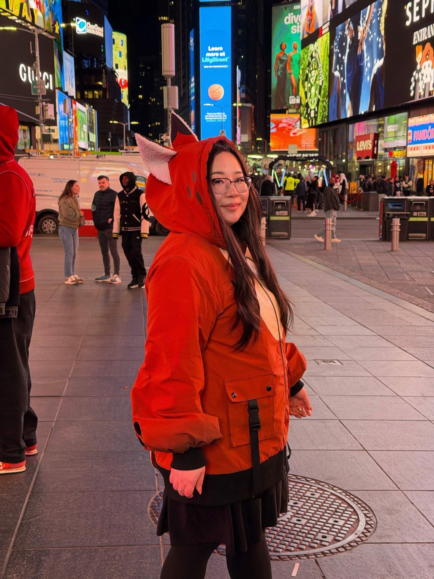 Model wearing a whimsical fox-inspired jacket with fox ears and oversized sleeves in Times Square at night.