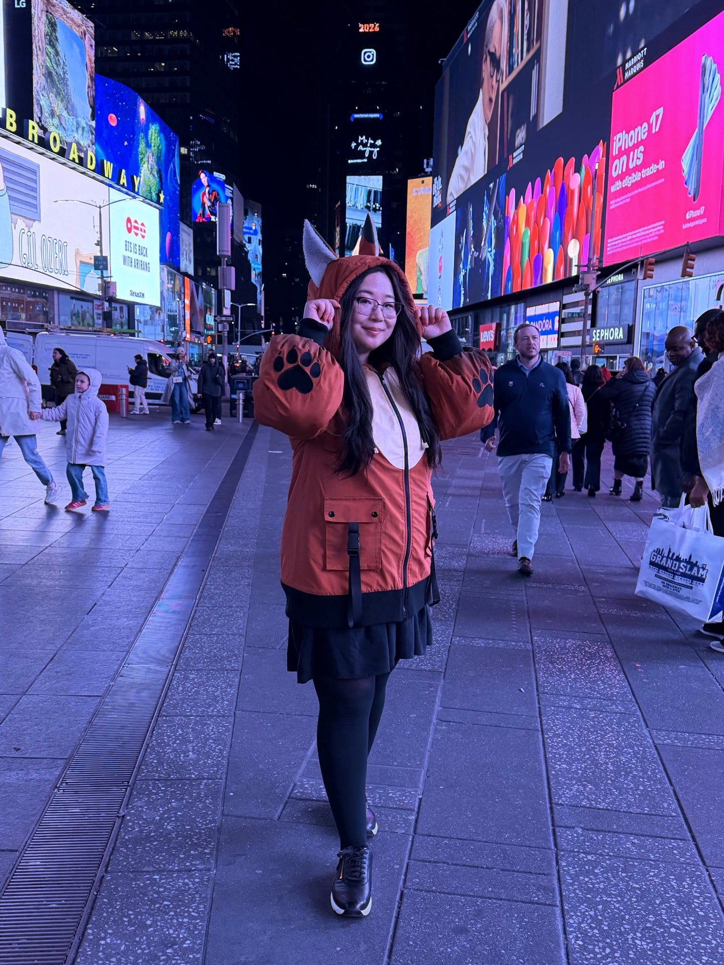 Model wearing a whimsical fox-inspired jacket with animal ears and paw print sleeves while posing in Times Square at night.