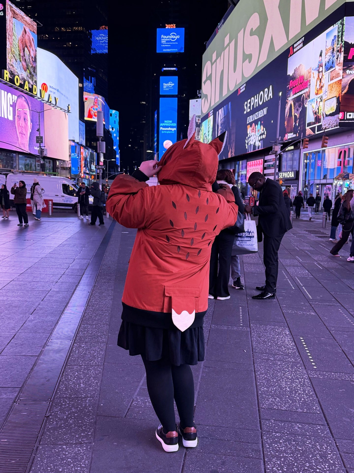 Back view of a whimsical fox-inspired jacket featuring animal ears, tail detail, and forest-inspired markings in Times Square at night.